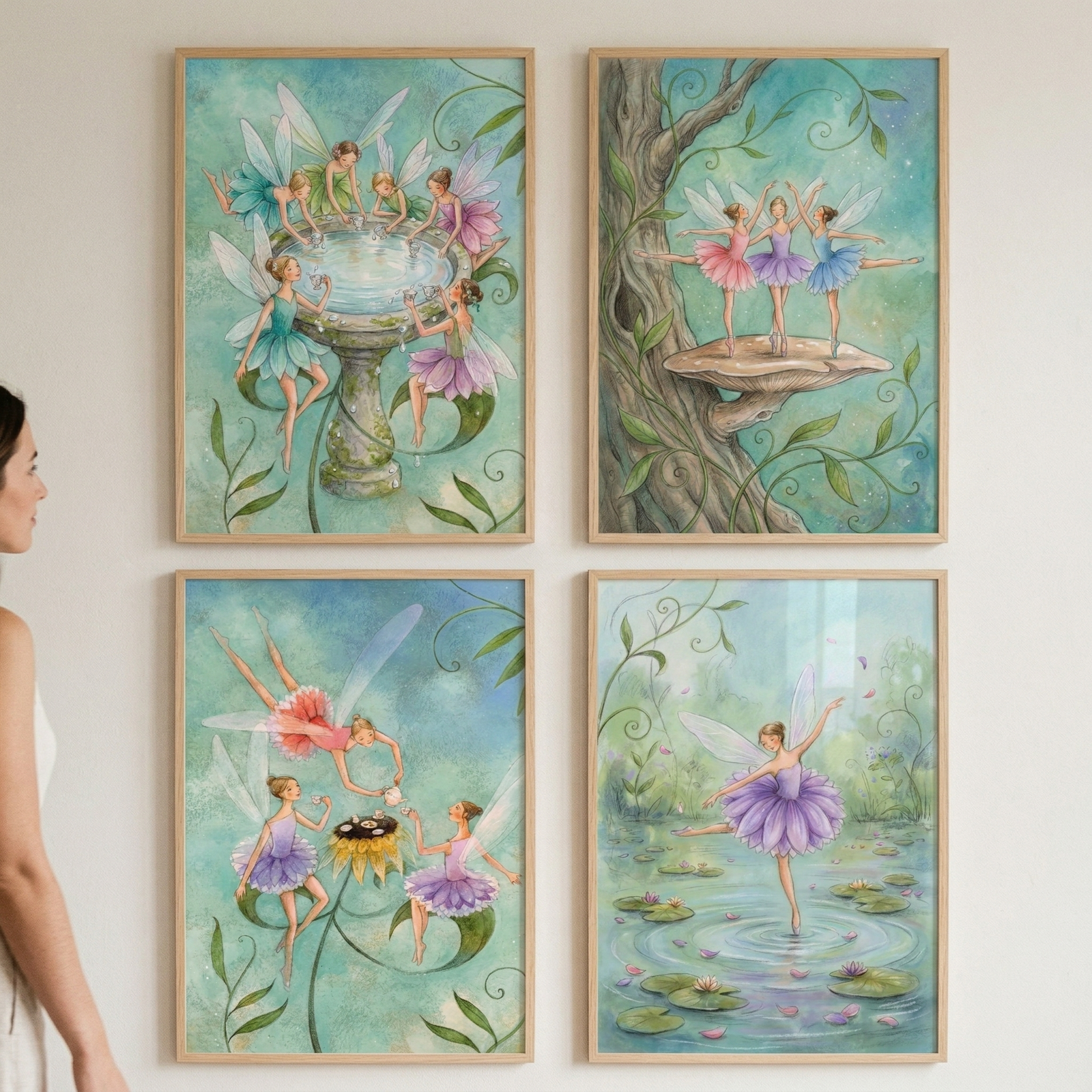 A woman stands to the left, viewing a set of four vertical, light-wood-framed illustrations displayed in a two-by-two grid on a plain white wall. The artwork features a whimsical theme of ethereal, winged figures with delicate features, dressed in colorful, ballet-inspired garments. The style is soft and illustrative, with a light pastel color palette dominated by greens, blues, and purples.
