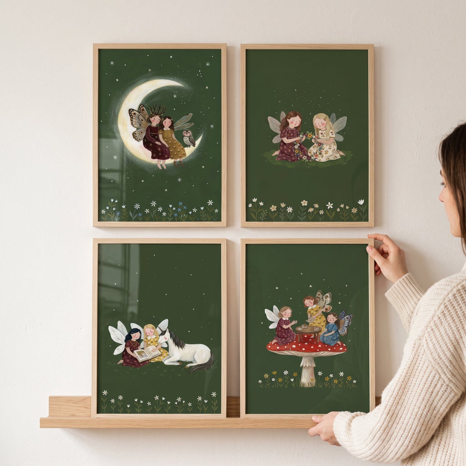 Forest green mythical fairies wall art set of 4 in wooden frames with fairies and a unicorn, being hung by a person.