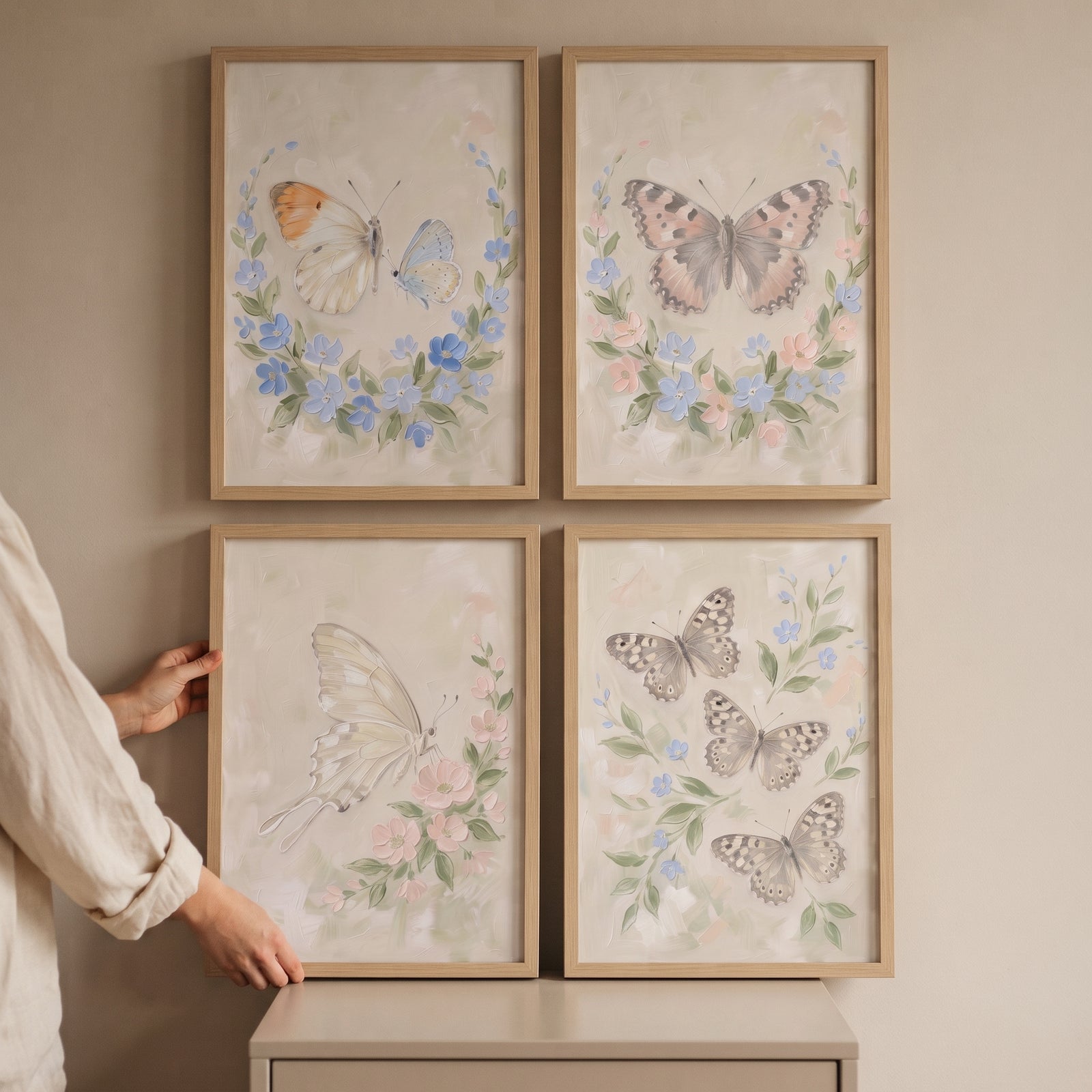 A person displays a four piece meadow butterfly wall art set of 4 with pastel insects and flowers in light wood frames.