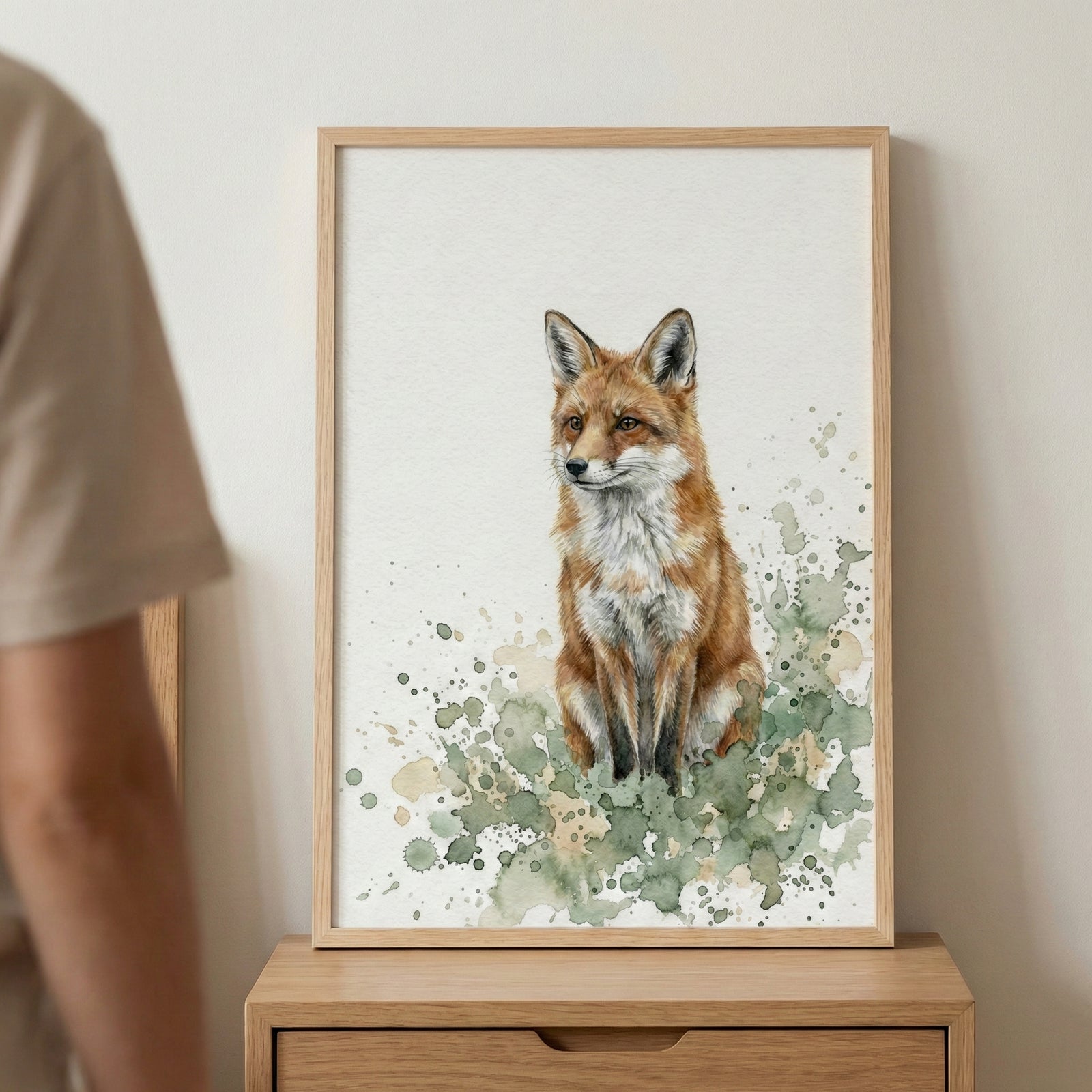 Close-up of a framed watercolor fox painting resting on a wood dresser, with a person's shoulder in the foreground.