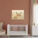 Modern nursery with terracotta walls. A white crib, cream armchair, and white dresser are visible. A framed illustration of a fox peeking through golden grasses hangs above the crib.
