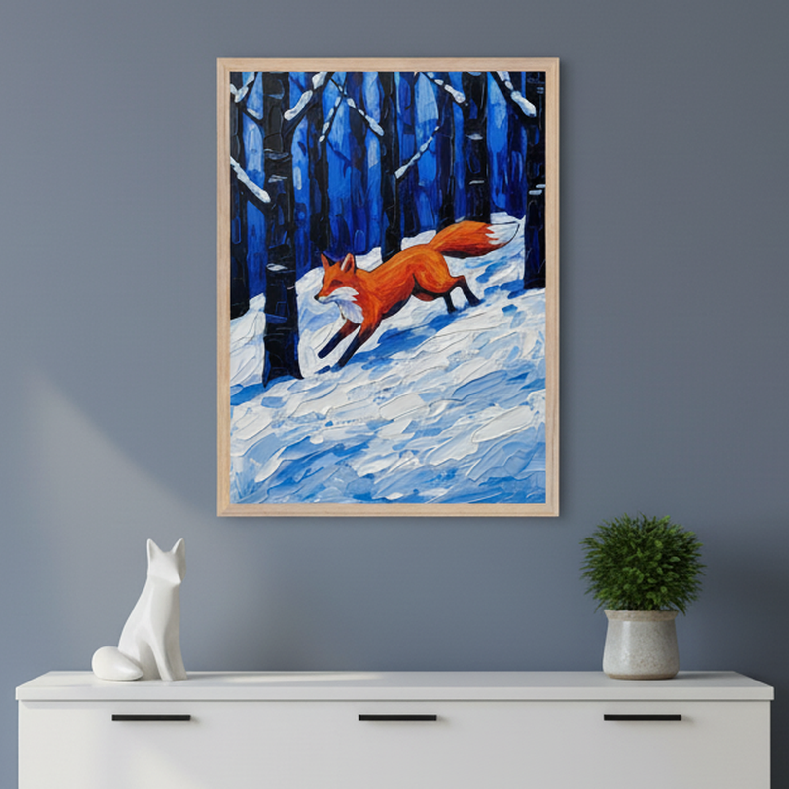 A framed painting of a vibrant red fox running through a snowy forest is displayed on a dark blue wall. The artwork uses bold brushstrokes and rich blues and whites to depict the wintry scene, with dark tree trunks adding depth and contrast to the fox’s motion.