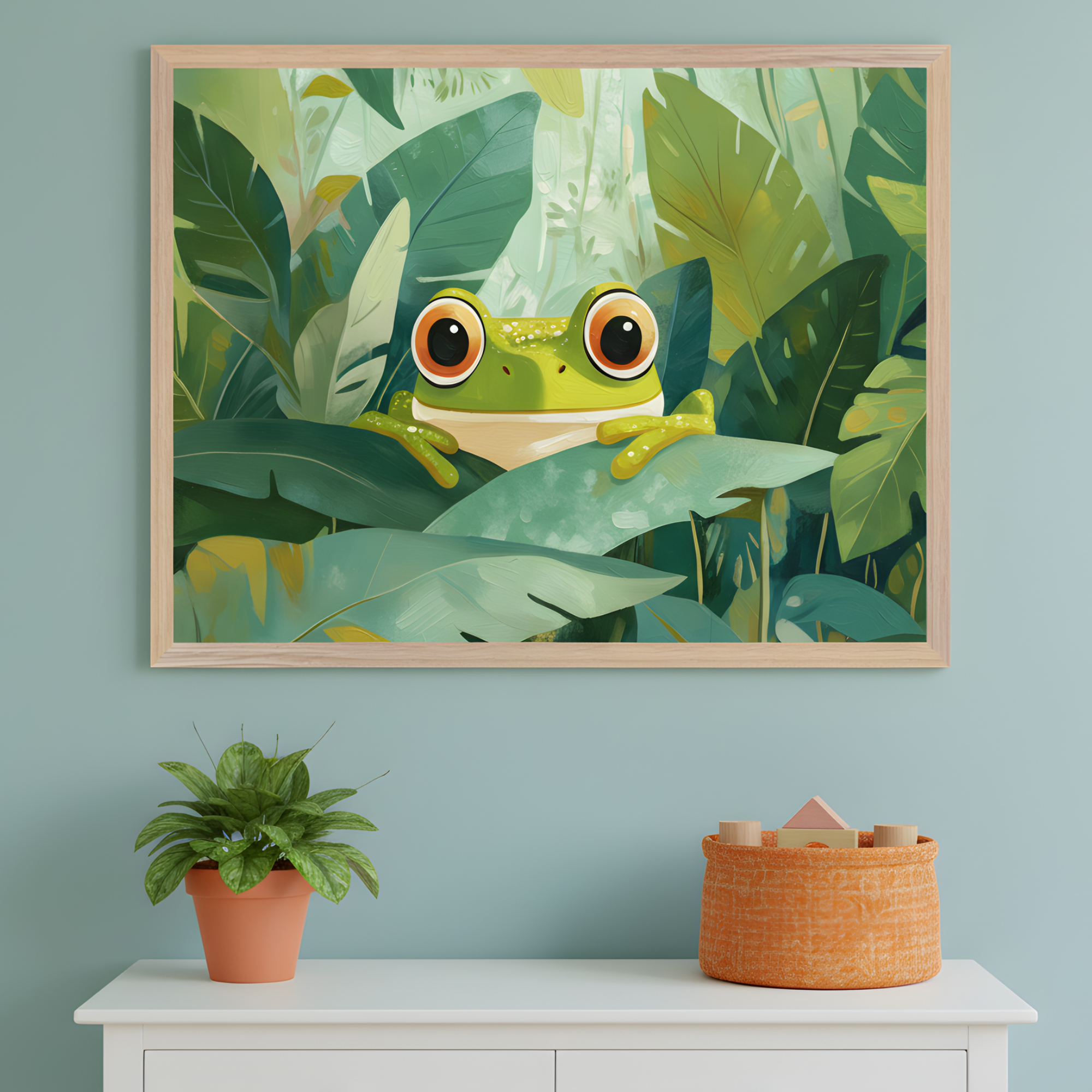 A whimsical framed illustration of a wide-eyed green frog peeking through lush jungle leaves, hanging on a light teal wall. Below the artwork sits a white dresser topped with a potted plant and an orange woven basket filled with wooden toys.