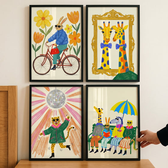 Funky maximalist dressed animal artwork set of 4 shows a cycling rabbit, giraffes, a disco leopard, and animals on a bench.