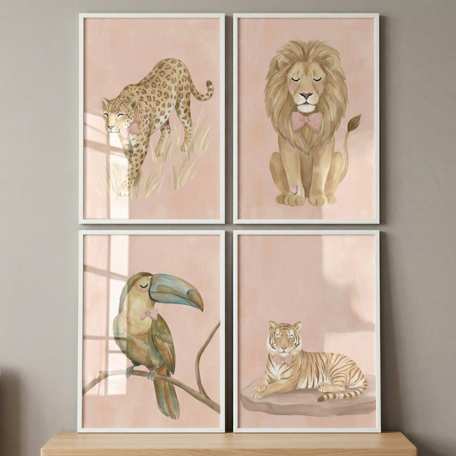 A set of four framed illustrations features whimsical safari animals in a soft, watercolor style. Each piece is set against a gentle pink background and features a different animal adorned with a delicate pink bow or bow tie.

