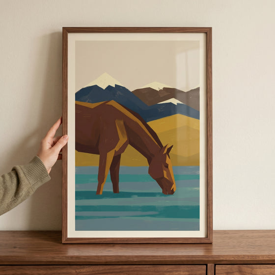Hand holds framed geometric teal water horse wall art of a horse drinking against a mountain landscape.