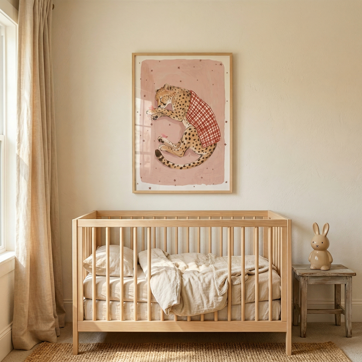 A serene nursery features a light wood crib with neutral linen bedding. Above it hangs a framed illustration of a spotted cheetah wearing a red-and-white checkered shirt on a dusty pink background. To the left, long beige curtains frame a window. On the right, a small weathered wooden stool holds a simple ceramic rabbit figurine. A textured woven rug covers the floor under the crib. The room is filled with soft natural light, creating a warm, minimalist aesthetic.