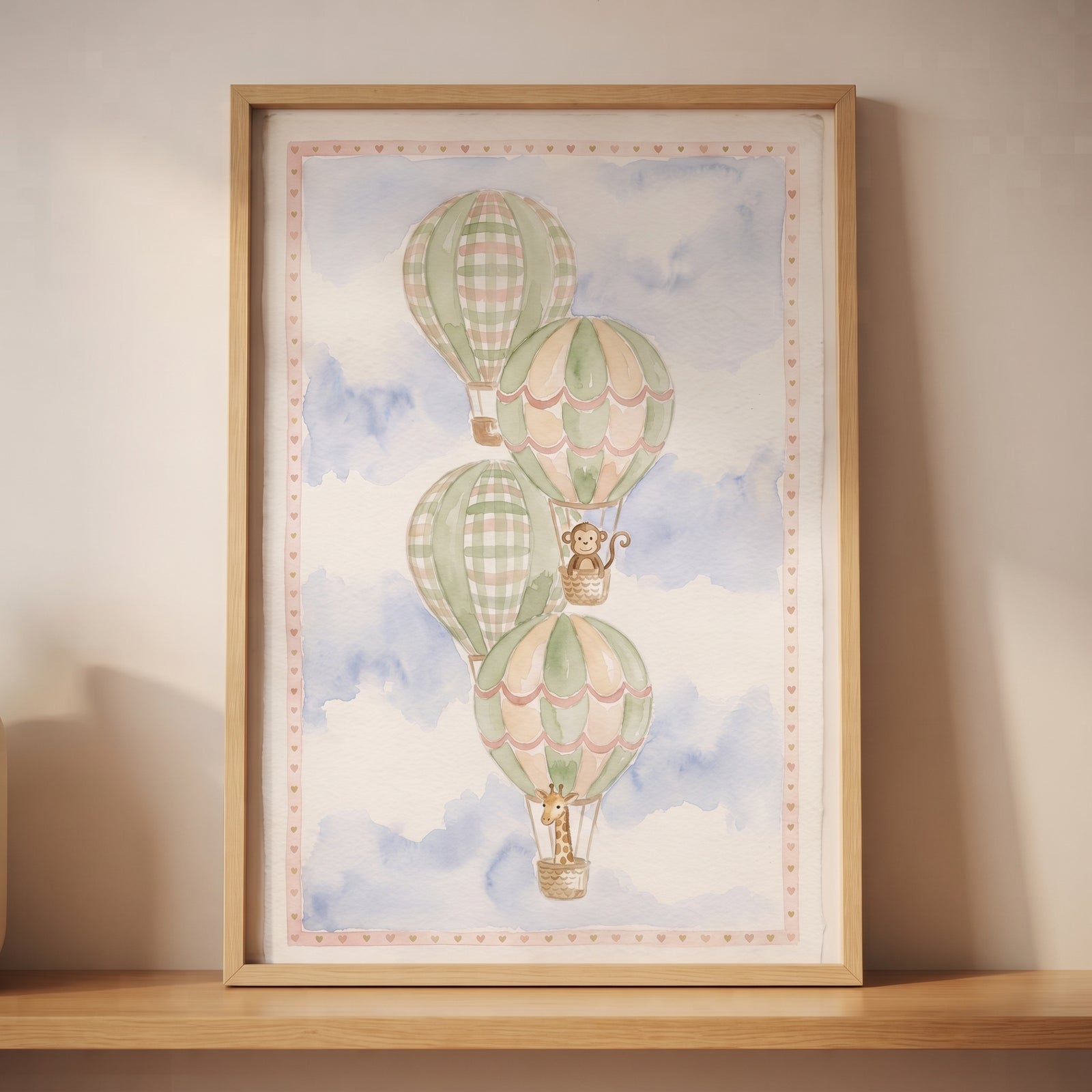 Watercolor gingham hot air balloon wall art with a monkey and giraffe in a blue sky, in a wooden frame on a shelf.