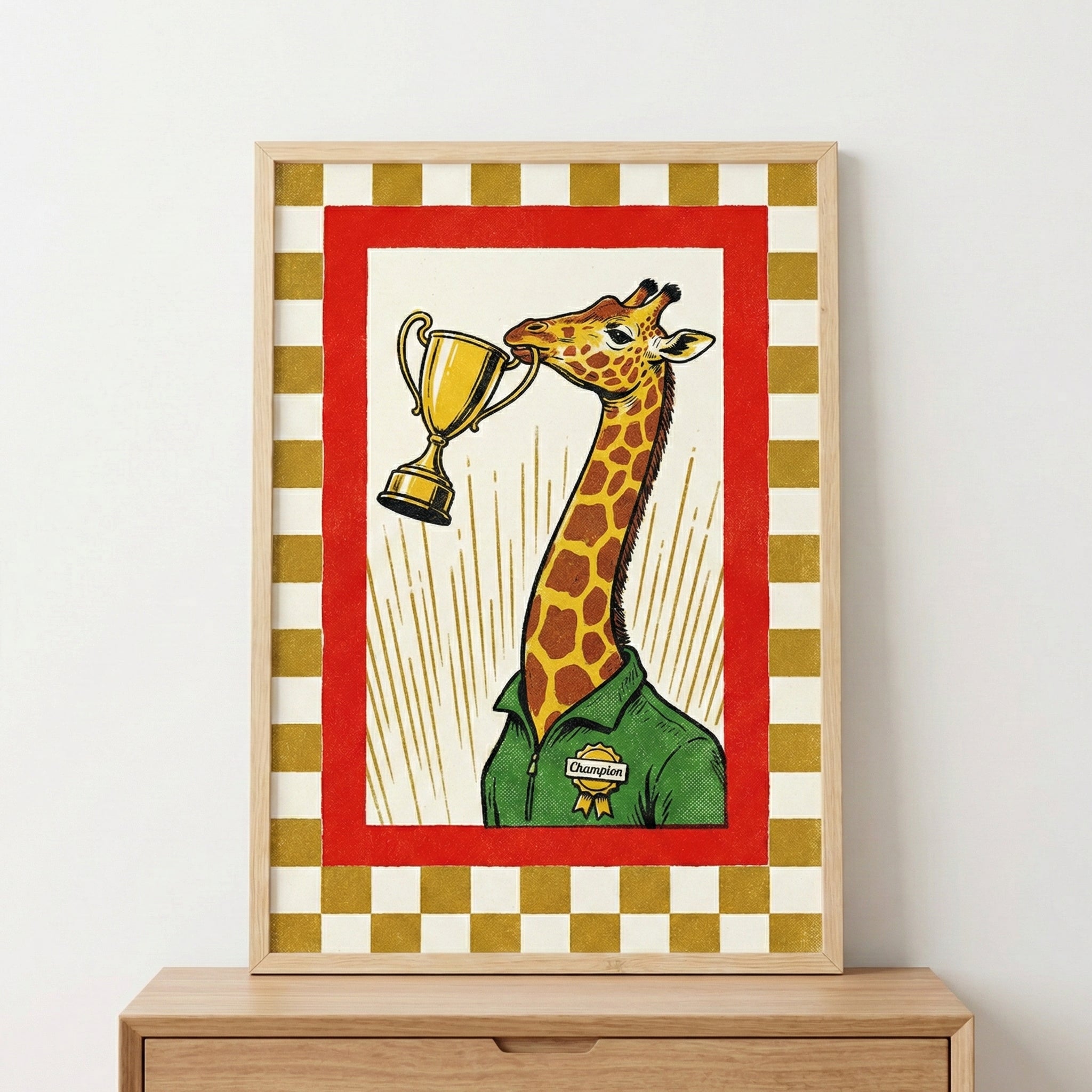 A framed graphic illustration features a giraffe wearing a green collared shirt with a yellow "Champion" badge. The giraffe holds a golden trophy cup in its mouth. Behind the giraffe are radiating yellow lines on a white background, all contained within a bold red frame. An outer border of gold and off-white checkered squares completes the design. The artwork is housed in a light wood frame, sitting atop a wooden dresser.
