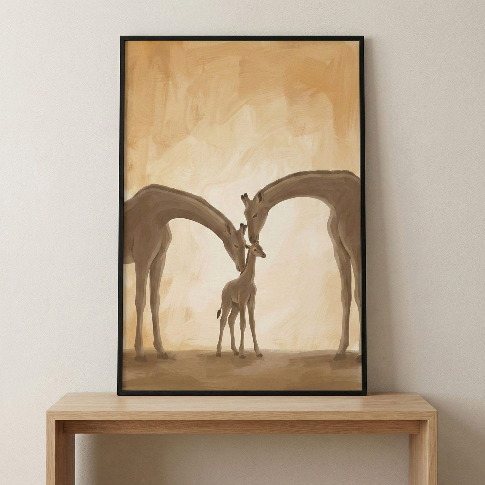 A vertical framed art piece sits on a light wood console table against a neutral wall. The illustration within the thin black frame depicts three giraffes in a tender, minimalist style. Two large giraffes stand on either side, their long necks gracefully arching inward so their heads can gently nuzzle a small giraffe calf positioned between them. 
