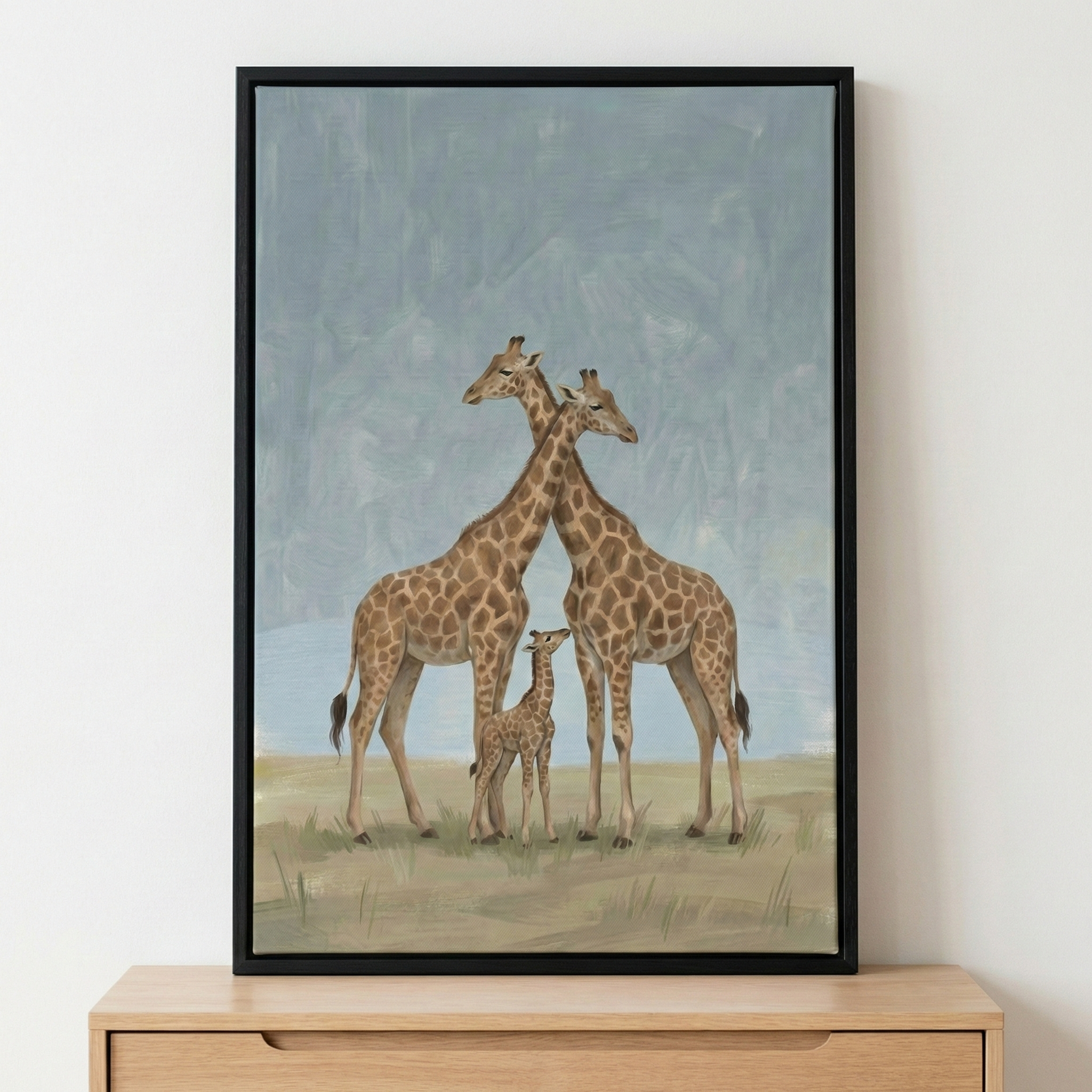 A framed artistic illustration captures a giraffe family in a minimalist landscape. Two tall adult giraffes stand side-by-side with their long necks gracefully crossing. A small calf stands positioned between the legs of the adults, completing the family portrait. The animals are depicted with traditional spotted patterns in shades of brown and tan. 