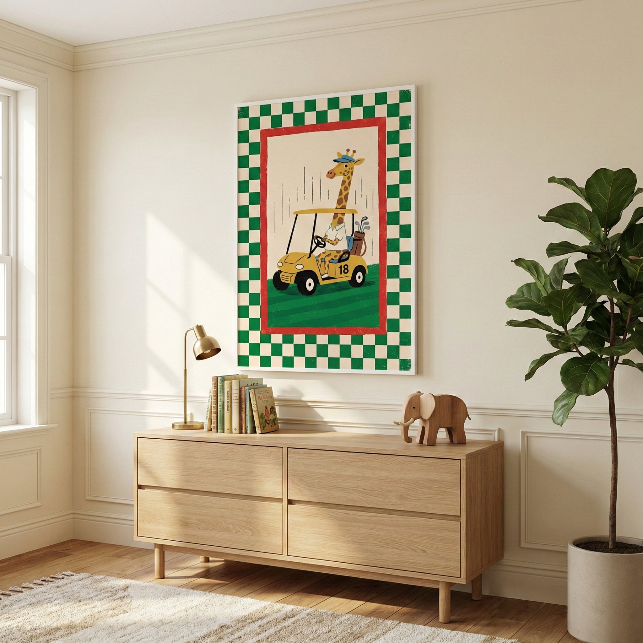 A bright, minimalist room features a light wood dresser with a large framed illustration hanging above it. The artwork depicts a whimsical cartoon giraffe wearing a hat and shirt while driving a yellow golf cart across a green field. The illustration is surrounded by a red inner border and a wide green-and-white checkered outer border. On the dresser sits a small brass lamp, a stack of books, and a wooden elephant figurine. 