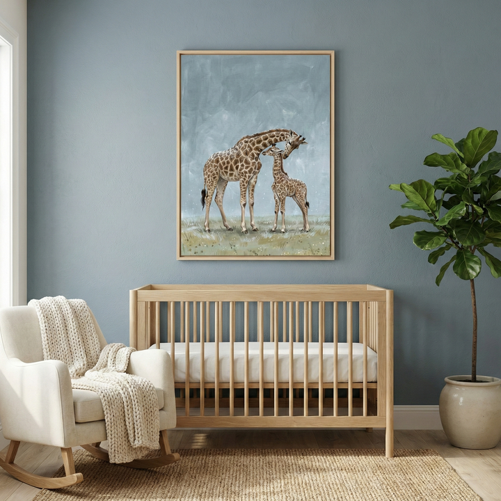 A serene nursery scene features a light-toned wooden crib centered against a muted blue wall. Above the crib hangs a large framed illustration of a tall giraffe and its smaller offspring in a gentle, affectionate pose. To the left, a white upholstered rocking chair is draped with a textured, cream-colored knit blanket. On the right side, a vibrant green potted plant adds a touch of nature. The entire room is anchored by a natural woven rug, creating a calm and inviting space.