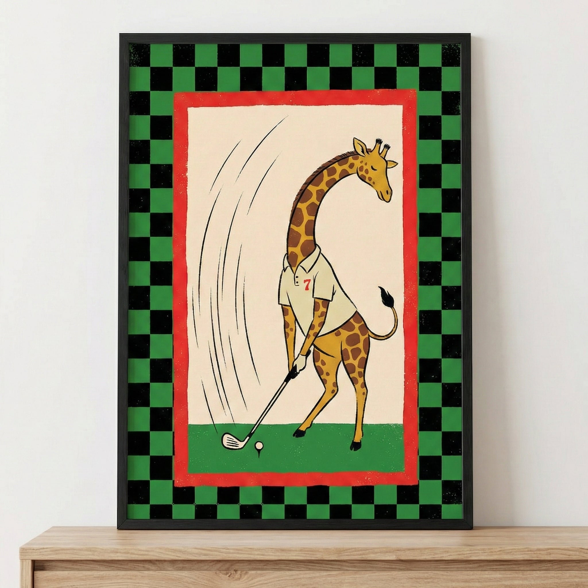 A framed illustration featuring a cartoon giraffe playing golf. The giraffe, depicted with its characteristic long neck and spots, is wearing a white collared shirt with a red number seven. It stands on green turf, holding a golf club and positioned to hit a white golf ball on a tee. Motion lines are drawn behind the giraffe to indicate a swing. This central scene is set on a cream-colored background with a red border, surrounded by a black and green checkered pattern. 