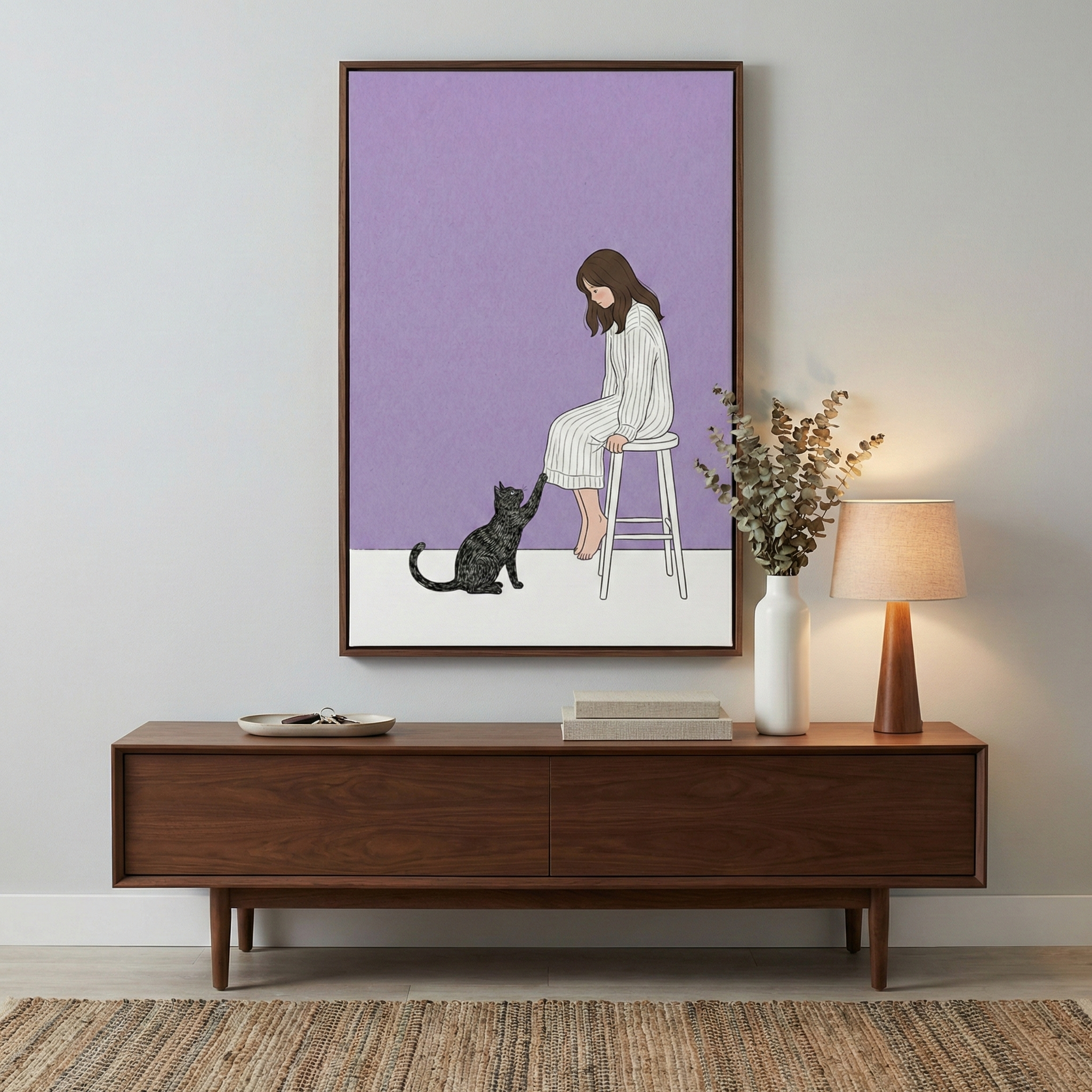 A vertical wooden frame displays a minimalist illustration centered on a light gray wall. In the illustration, a woman with long brown hair sits on a white stool, looking down at a dark tabby cat that is reaching up towards her. The background of the illustration is split into a lavender upper portion and a white lower portion. Below the artwork sits a long, mid-century modern sideboard crafted from dark brown wood. 
