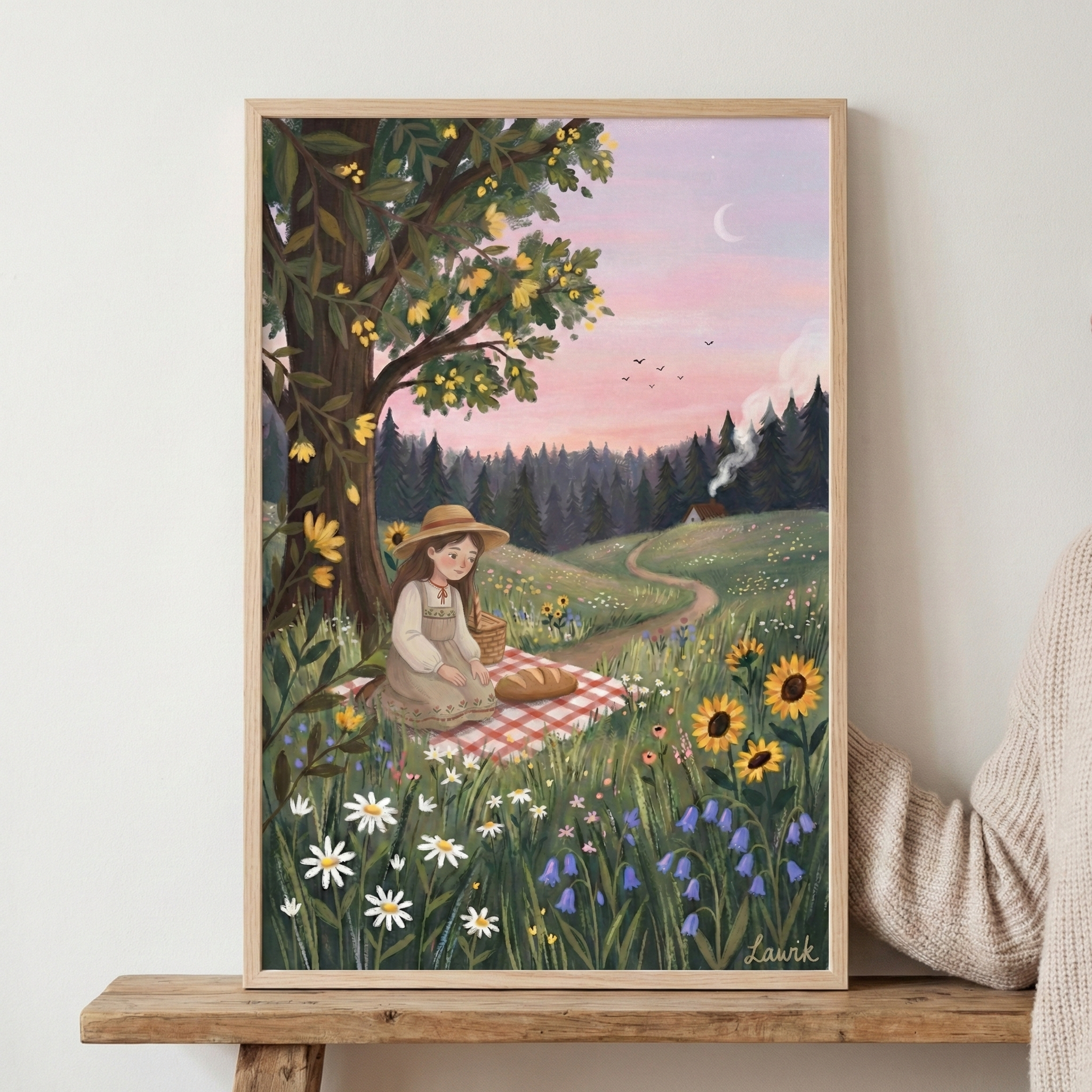 A whimsical folk-style illustration of a young girl with long brown hair wearing a straw hat and simple dress. She sits on a red-and-white checkered picnic blanket under a large, leafy tree. A loaf of bread and a basket rest beside her. The foreground is a lush meadow of sunflowers, daisies, and bluebells. In the background, a winding path leads past a small cottage with a smoking chimney toward a dark evergreen forest under a soft pink sunset sky with a crescent moon and distant birds.