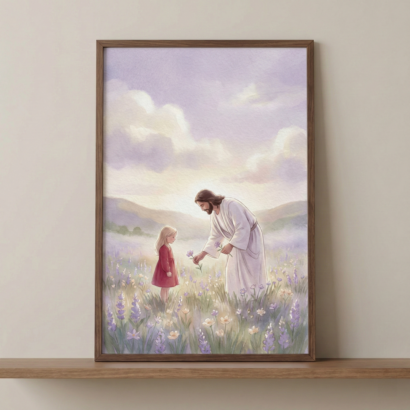 A framed illustration rests on a wooden shelf against a plain wall. The artwork depicts Jesus with long brown hair and a beard, wearing a flowing white robe. He is bending down to gently hand a purple wildflower to a young girl with blonde hair wearing a red dress. They stand in a vast meadow filled with purple and yellow flowers. The background features rolling hills beneath a soft, pastel sky with clouds in shades of lavender and cream. The style is light and soft.