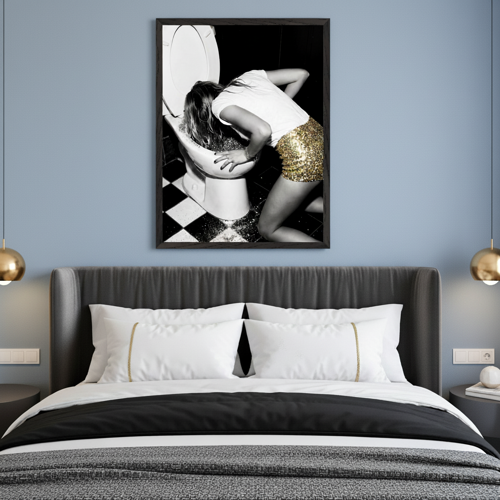 Modern bedroom with a dark gray upholstered bed. A framed black and white photograph of a woman in a white shirt and gold sequined skirt vomiting into a toilet hangs above the bed.