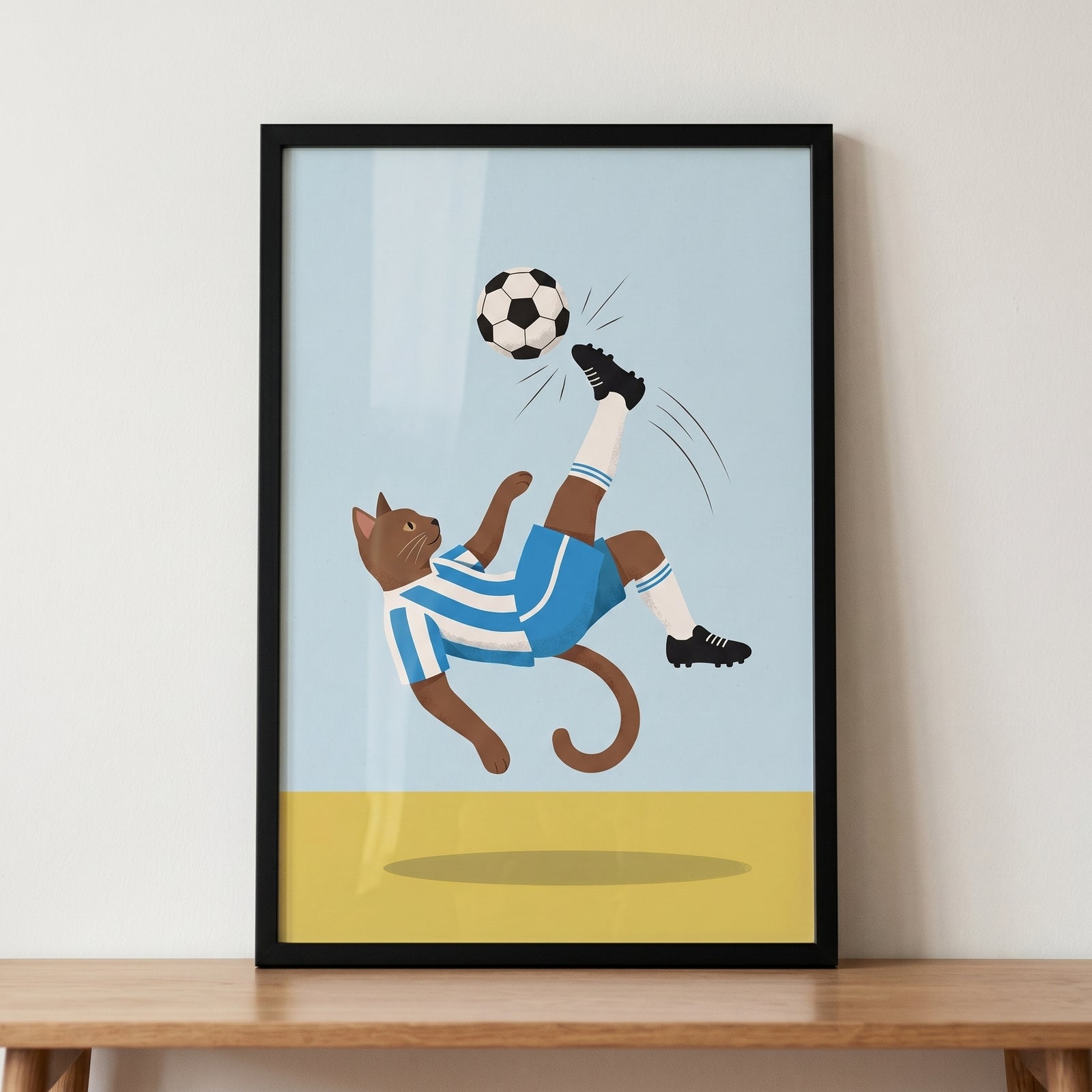 Goal kick soccer cat wall art shows a brown cat in a blue and white kit performing a bicycle kick in a black frame.