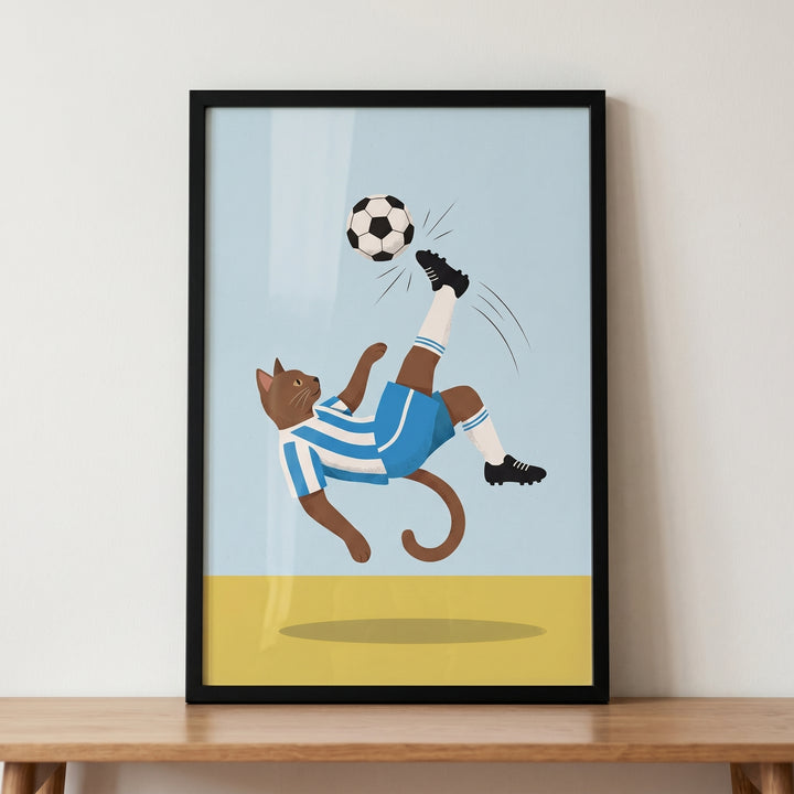 Goal kick soccer cat wall art shows a brown cat in a blue and white kit performing a bicycle kick in a black frame.