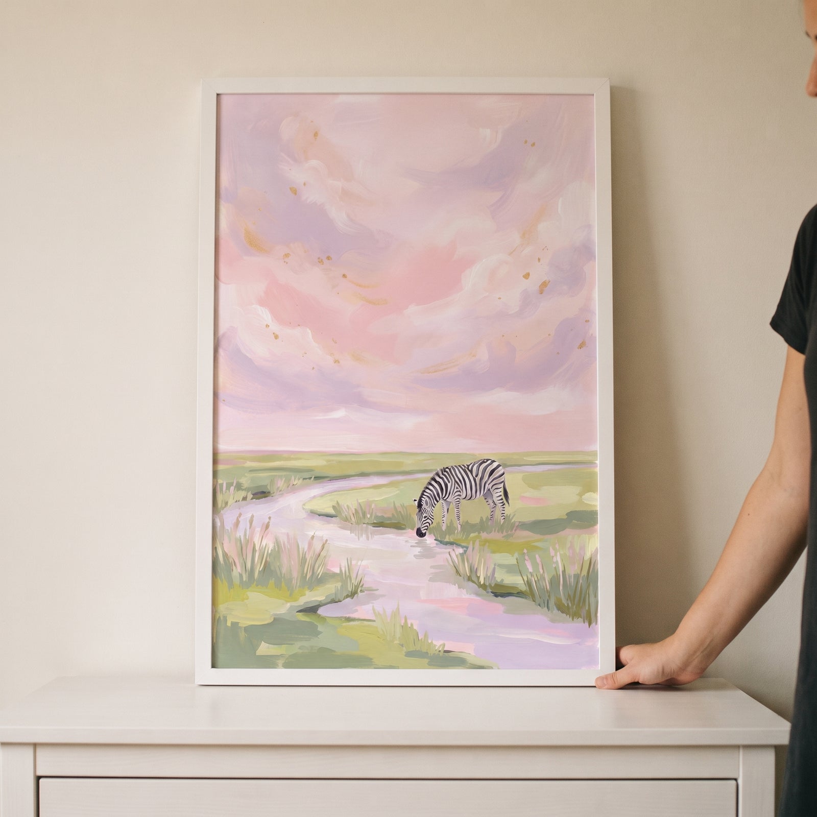 Framed gold flecked sky zebra animal wall art shows a zebra drinking from a stream under soft pink and purple clouds.