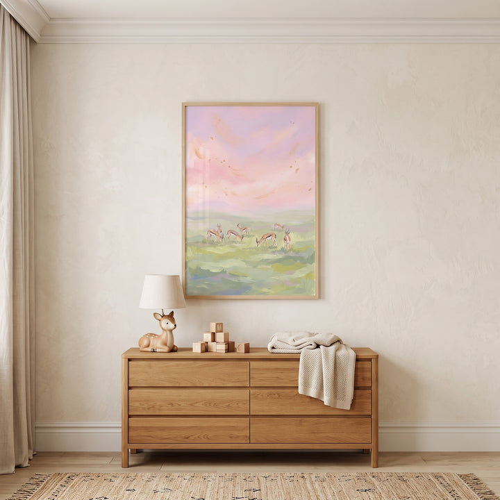 Framed gold leaf sky springbok animal print hangs above a wooden dresser with a deer lamp and blocks in a neutral nursery.