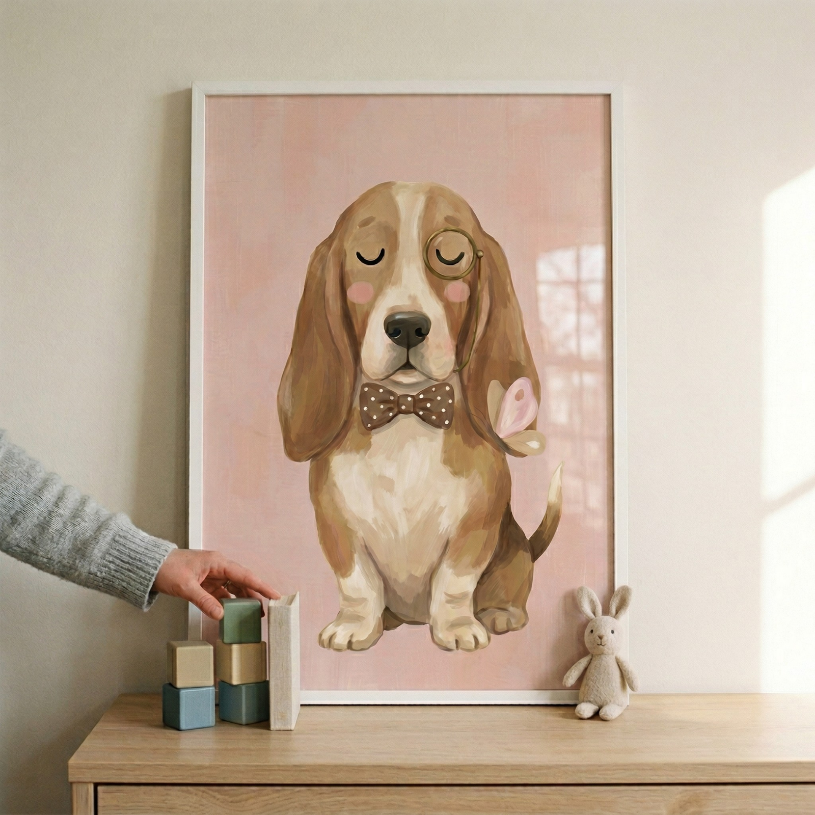 A vertical, white-framed illustration is the central focus, resting on a light-toned wooden surface against a neutral-colored wall. The artwork depicts a light brown and white dog, characterized by long, drooping ears and a gentle expression with its eyes closed. The dog is accessorized with a gold-colored monocle over its left eye and a brown bow tie featuring white polka dots. Small pink circles accentuate its cheeks, and a tiny pink butterfly is perched on its left ear.