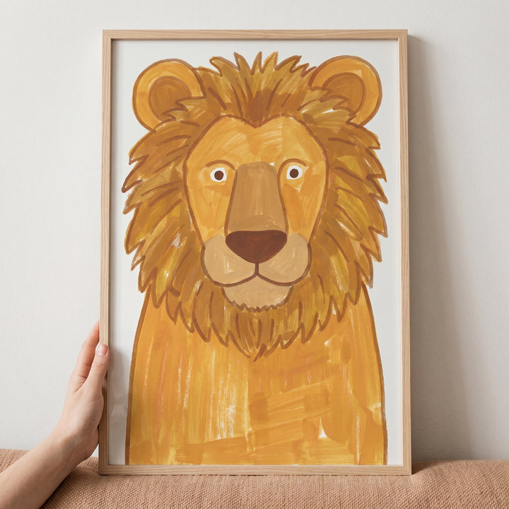 Hand holding a light wood frame with a friendly lion illustration, golden lion wall art.