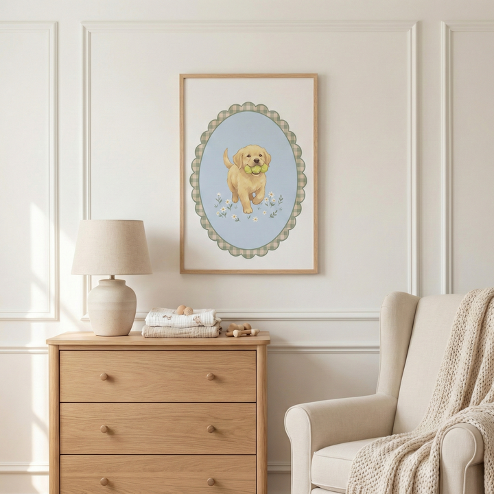 This image displays a neutral-toned nursery or child's bedroom. Centered on a white wall with decorative molding is a framed illustration of a small golden puppy. The puppy is depicted holding a bright yellow ball in its mouth, surrounded by delicate white flowers within a scalloped oval border on a light blue background. The frame itself is a simple, light wood.

