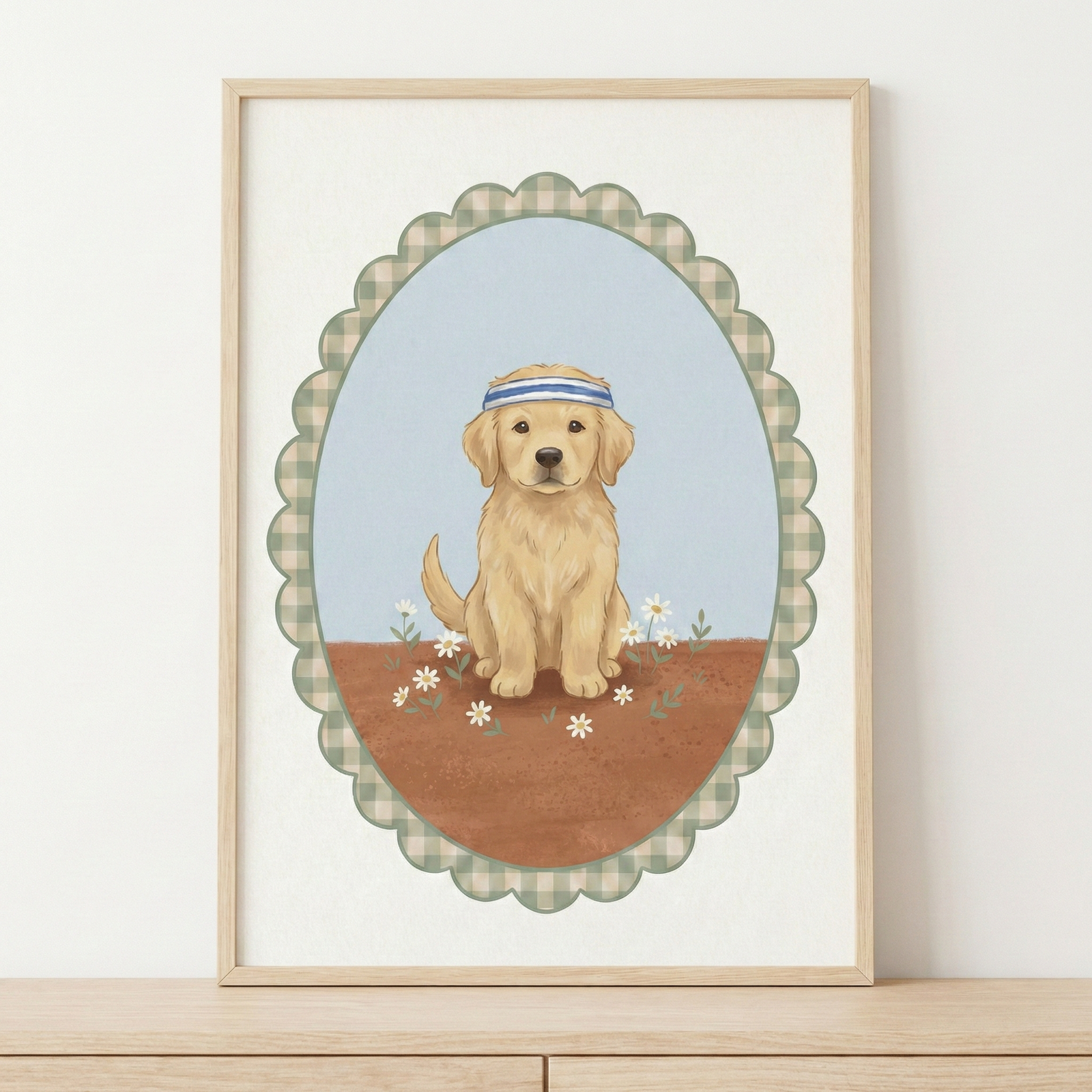 A charming illustration features a golden retriever puppy sitting forward, wearing a blue and white striped headband. The puppy is placed on reddish-brown ground dotted with small white daisies, set against a pale blue sky. This scene is contained within a scalloped oval border that features a green and white checkered pattern. The entire artwork is centered on a clean white background and displayed in a simple light wood-toned frame resting on a wooden surface.