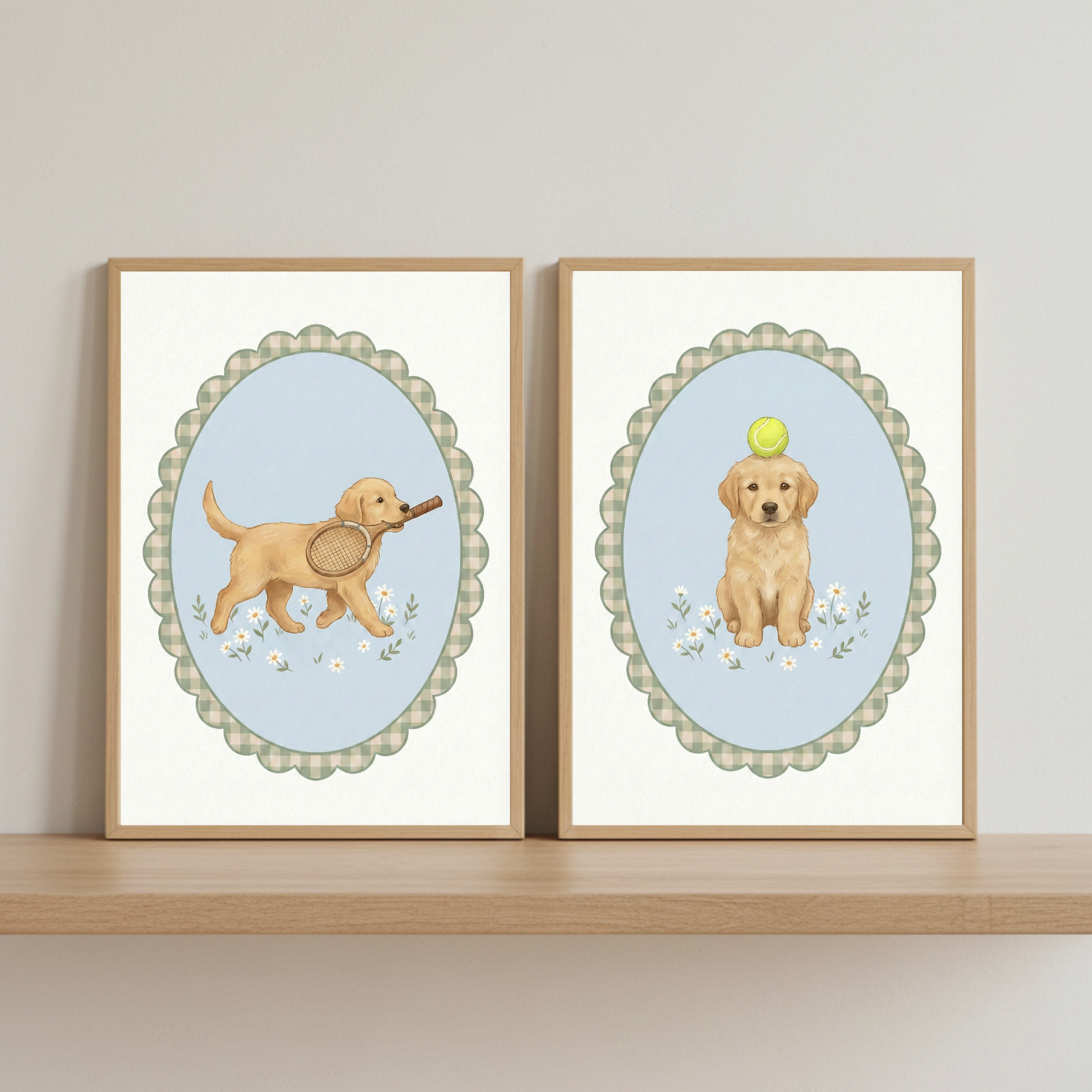 Two framed illustrations of a golden retriever puppy rest side-by-side on a light wood shelf against an off-white wall. Each piece is encased in a simple wood frame. Within the frames, the artwork is centered inside a scalloped oval border featuring a green and white gingham pattern. The left image shows the puppy walking while holding a tennis racket in its mouth. The right image depicts the puppy sitting with a green tennis ball balanced on its head. The style is soft and whimsical.