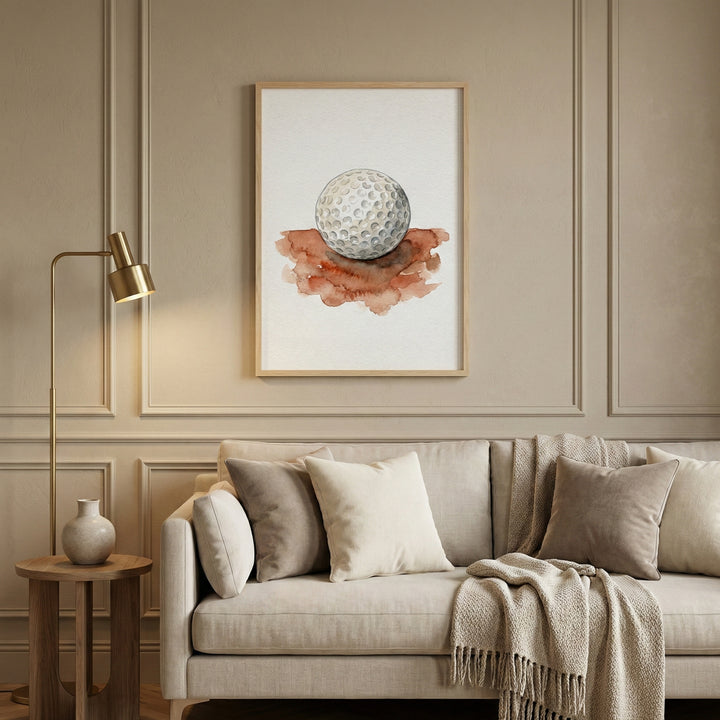 Framed artwork of a golf ball painted in soft neutral tones, hanging above a beige couch in a stylish living room. The image blends athletic focus with serene interior design.