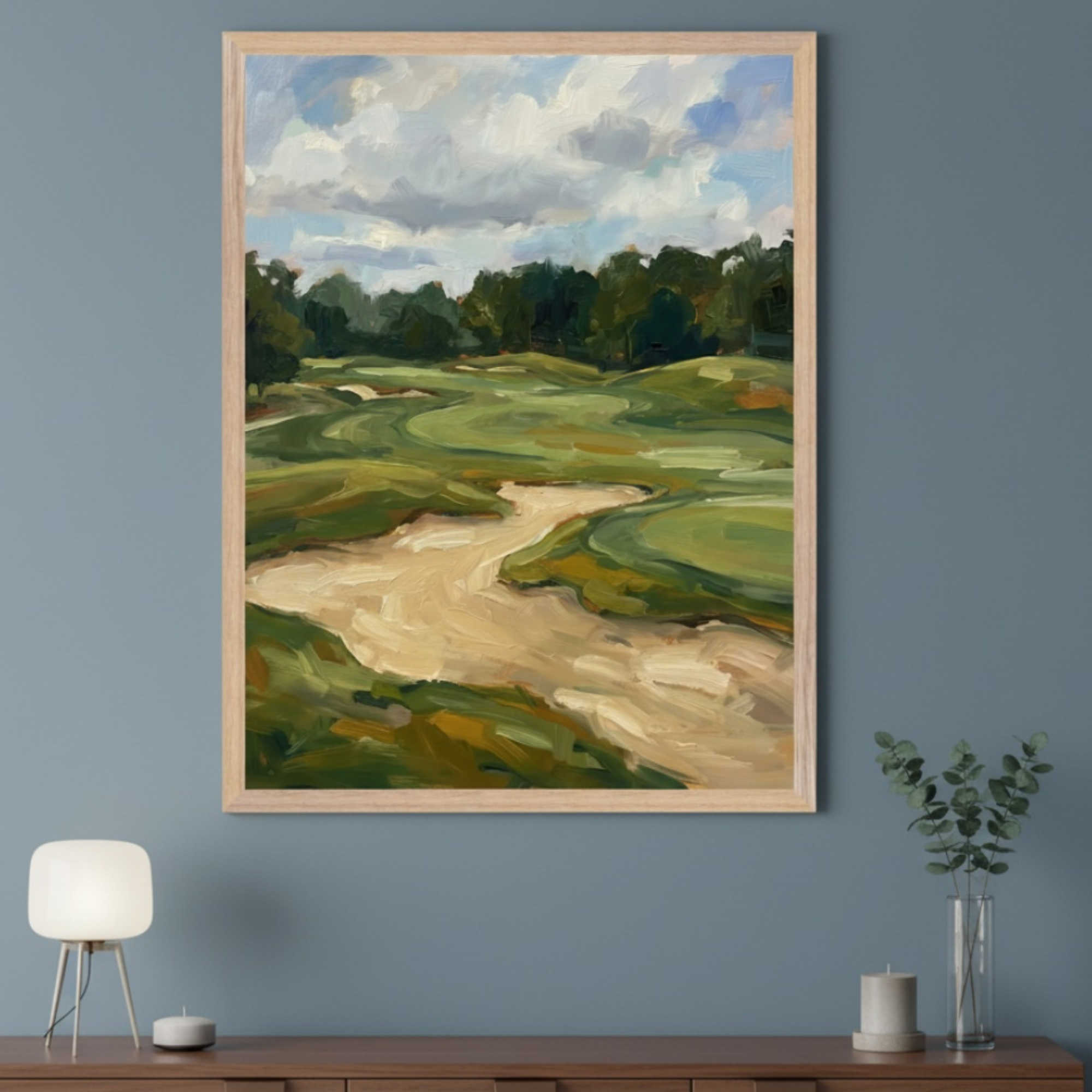Modern room with a wooden console table. A large, light wood framed oil painting of a golf course with green fairways and sand traps hangs centered above the console table. A lamp and vase are on the table.
