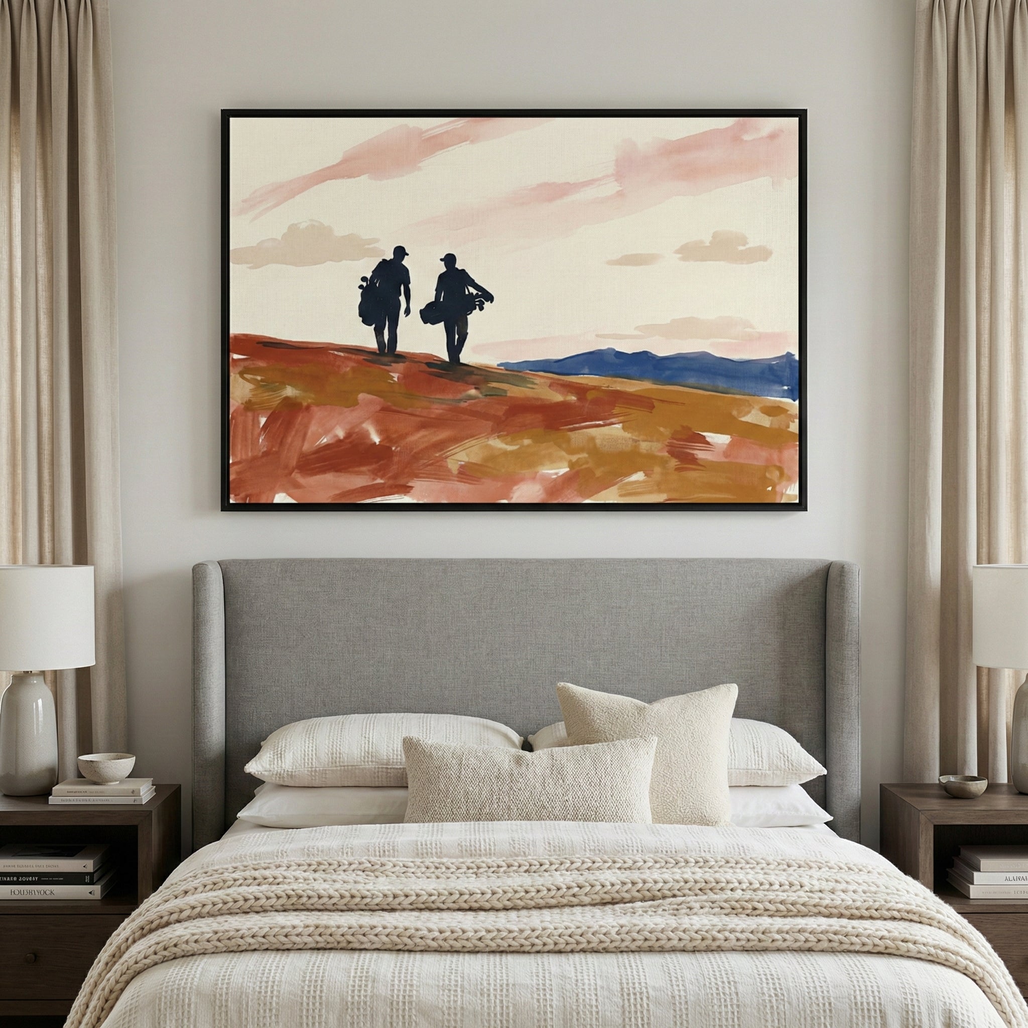 A minimalist bedroom featuring a bed with a grey upholstered headboard and layered neutral-toned bedding. On either side are matching wooden nightstands topped with modern lamps. Hanging above the bed is a large framed horizontal piece of art depicting two silhouetted figures walking across a reddish-brown landscape under a soft pink and white sky. Long, cream-colored curtains frame the scene on both sides against light-colored walls.