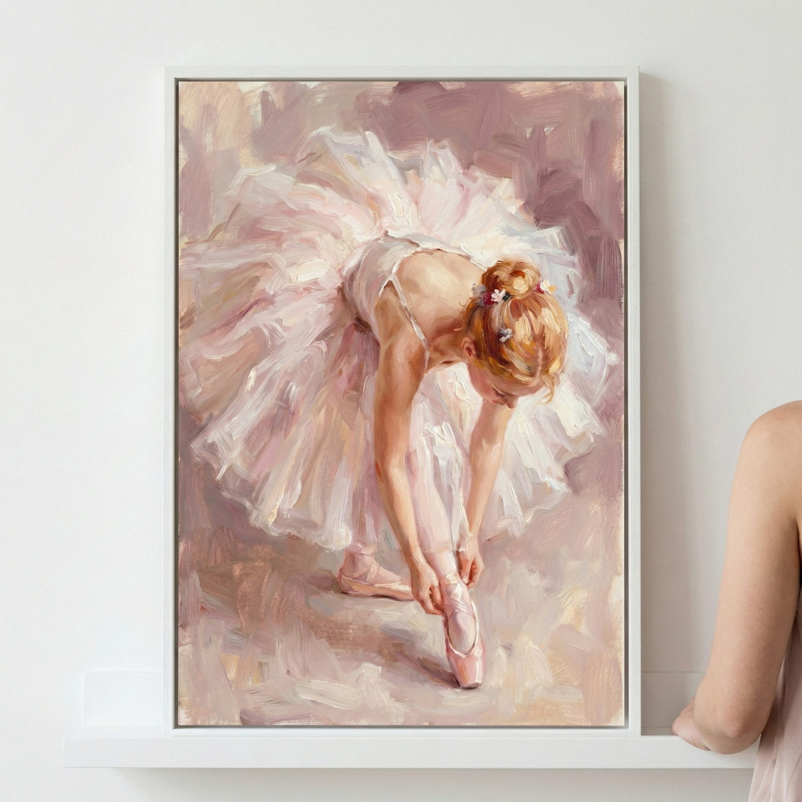 A person stands beside a framed painting of a ballerina adjusting her pink pointe shoes, wearing a delicate white tutu, against a soft, pastel background.