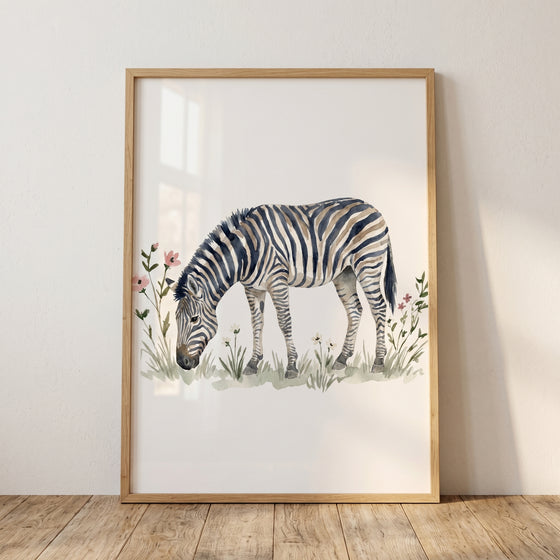 Framed grazing meadow zebra wall art showing a zebra in a field of flowers, leaning against a wall on a wood floor.