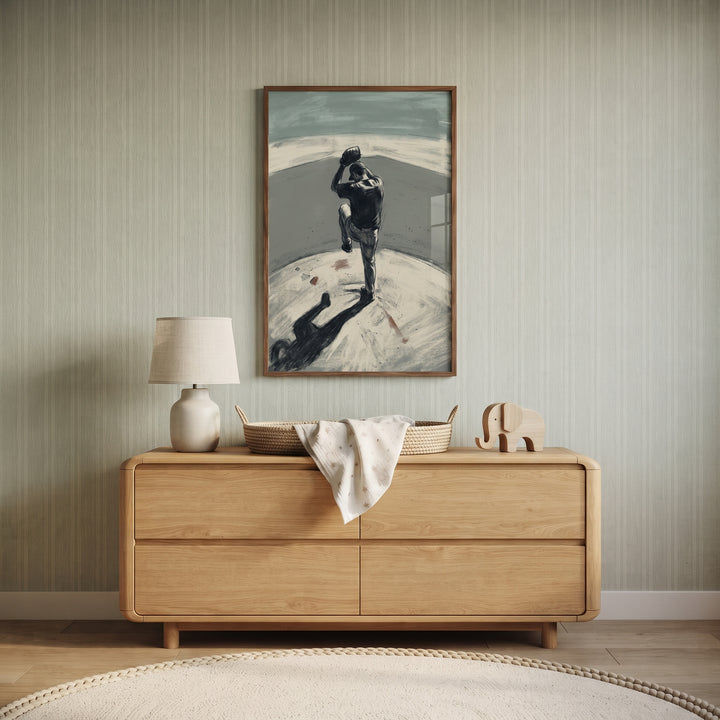 Grey baseball pitcher sports wall art hangs on a striped wall above a light wood dresser in a nursery.