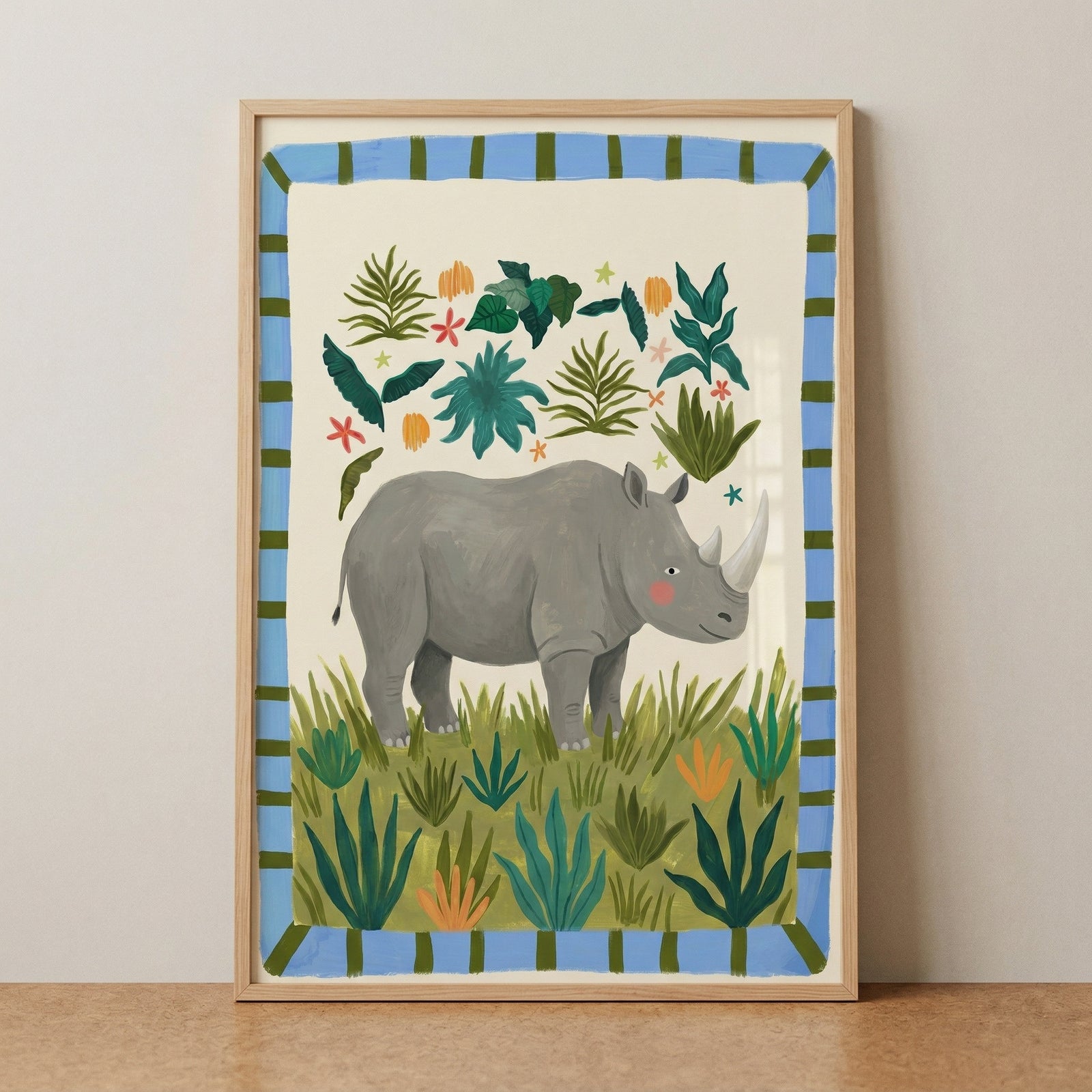 Framed illustration of a gray rhinoceros standing among green grass and leafy plants with small colorful flowers scattered around. The soft cream background and blue striped border create a playful jungle themed print with a calm and friendly feel.