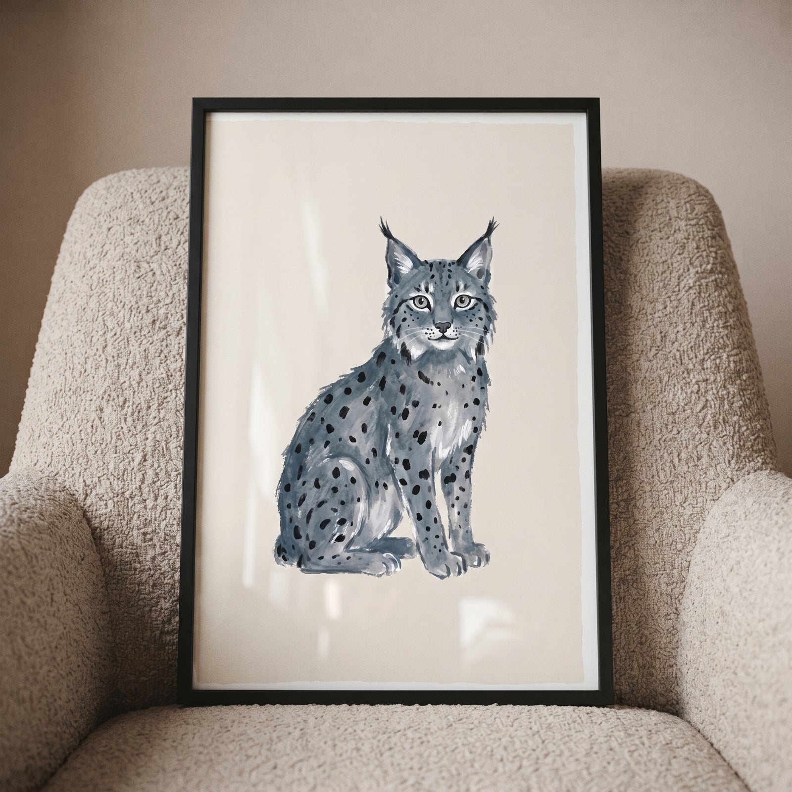 Grey tufted ear lynx artwork in a black frame resting on a textured beige armchair.