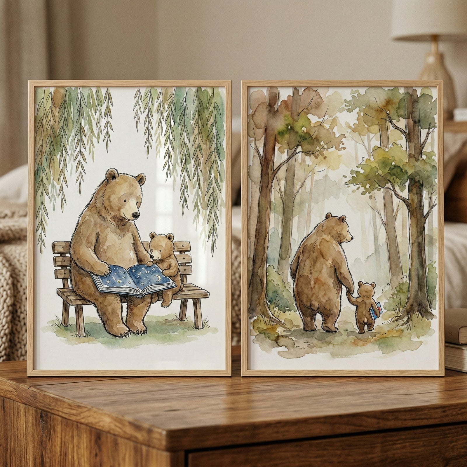 Two framed watercolor-style illustrations rest on a wooden surface. In the first, a large brown bear sits on a wooden bench beside a small bear cub. The large bear holds an open book with a blue, star-patterned cover. Above them, green willow branches hang down. In the second, the two bears are seen from behind, holding hands as they walk into a sun-dappled forest of tall trees. The small cub carries a blue book. Both pieces feature soft tones and a whimsical, gentle feel.