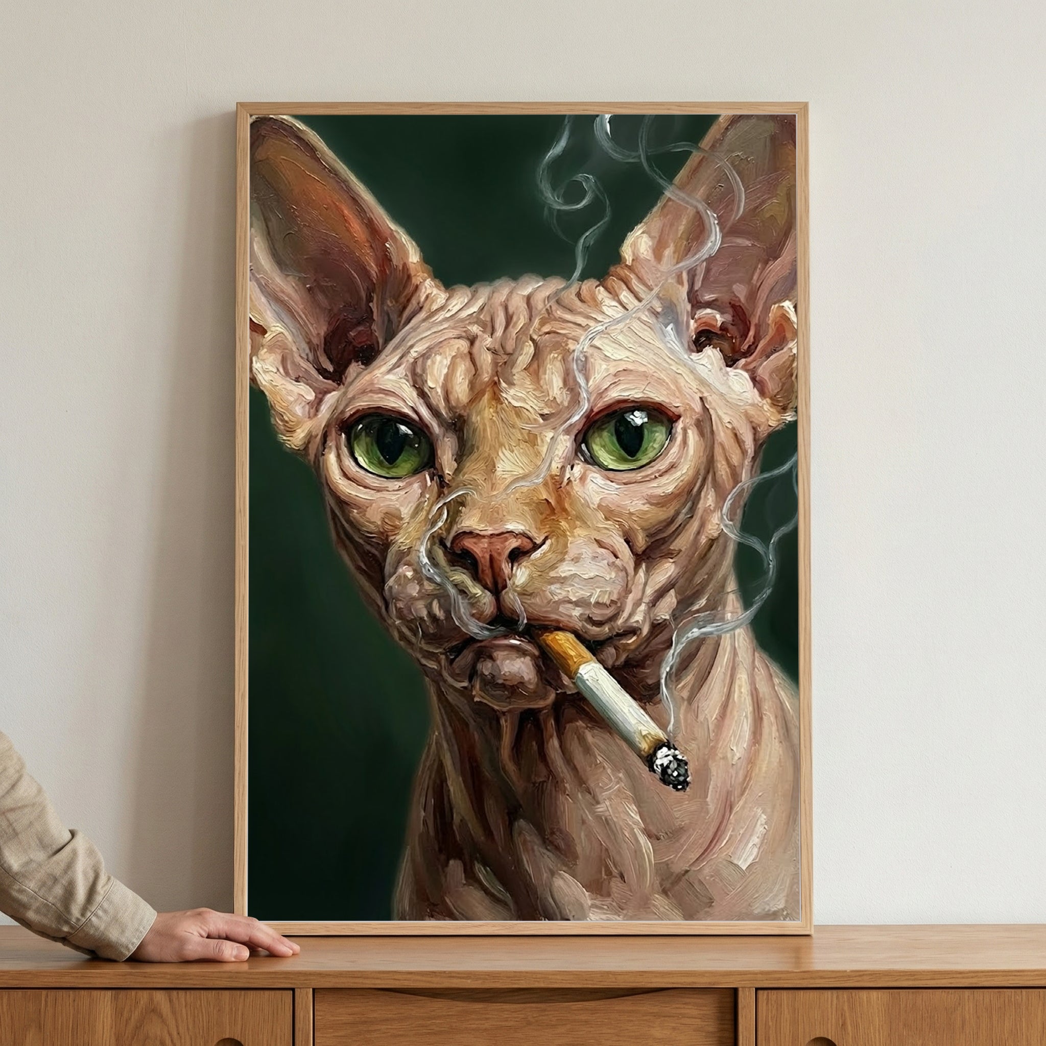 A close-up, textured illustration of a hairless cat with large, expressive green eyes and deeply wrinkled skin. The cat holds a lit cigarette in its mouth, with swirling wisps of white smoke curling around its face against a dark green backdrop. The framed portrait is mounted on a plain wall above a wooden sideboard.