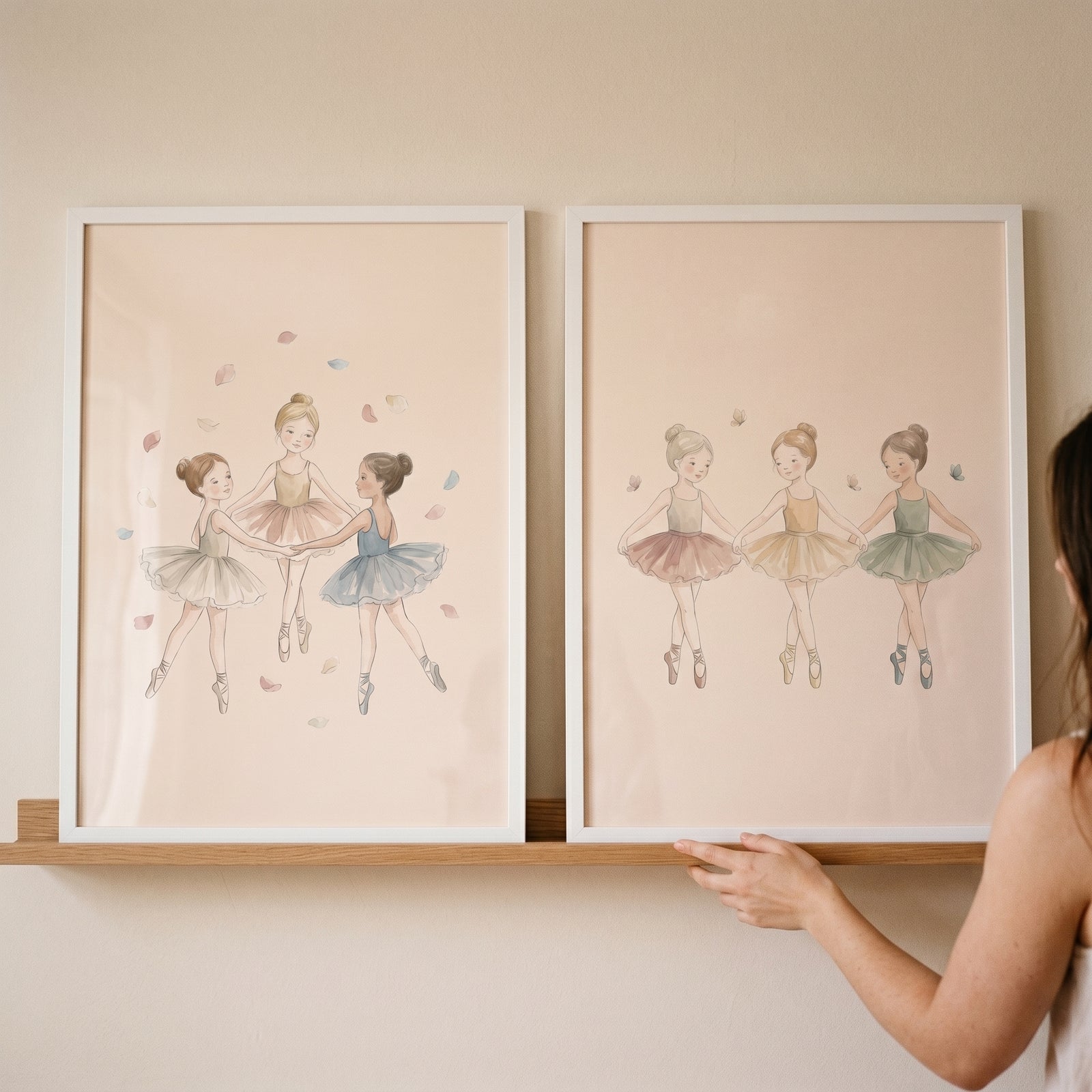 A hand holding dancing ballerina wall art set of 2 on a wooden shelf, showing young dancers in soft pastel tutus.