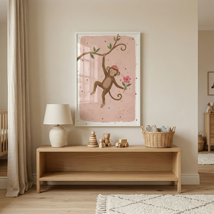 A cozy and minimalist nursery or child's bedroom is decorated in soft, neutral tones. Centered on the beige wall is a large white-framed vertical illustration featuring a whimsical brown monkey wearing a small red cap. The monkey hangs by one arm from a branch and holds a pink flower against a light pink background dotted with tiny details. 