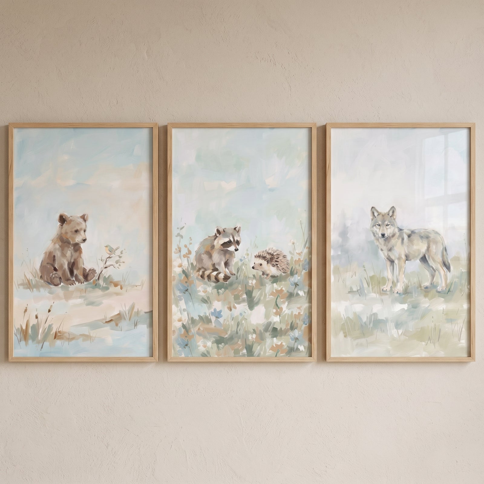Hazy blue woodland animals wall art set of 3 featuring a bear cub, raccoon, hedgehog, and wolf in light wood frames.