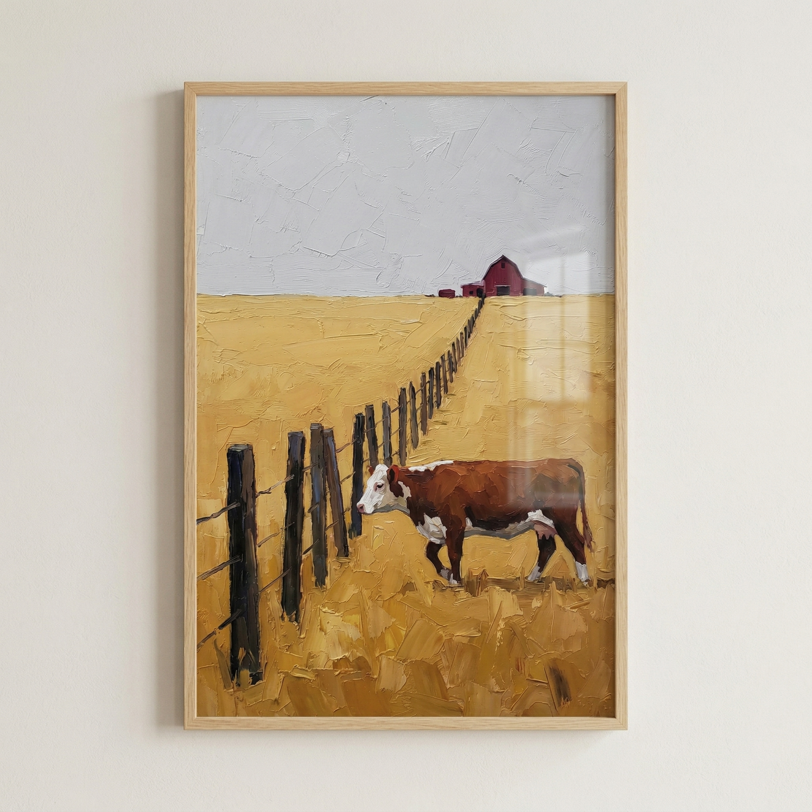 Framed artwork featuring a brown and white cow standing in a vast, textured golden field. A dark post-and-rail fence creates a leading line from the foreground toward a small red barn on the horizon under a muted grey sky. The piece has a thick, impasto-style texture with visible, expressive strokes that give the landscape a tactile feel. The overall color palette is dominated by warm ochre and yellow tones, contrasted by the dark fence and the small pop of red in the distance.