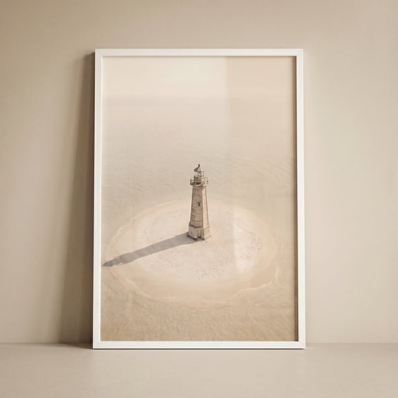 High key minimalist lighthouse wall art in a white frame showing a solitary tower on a circular sandbar in beige tones.