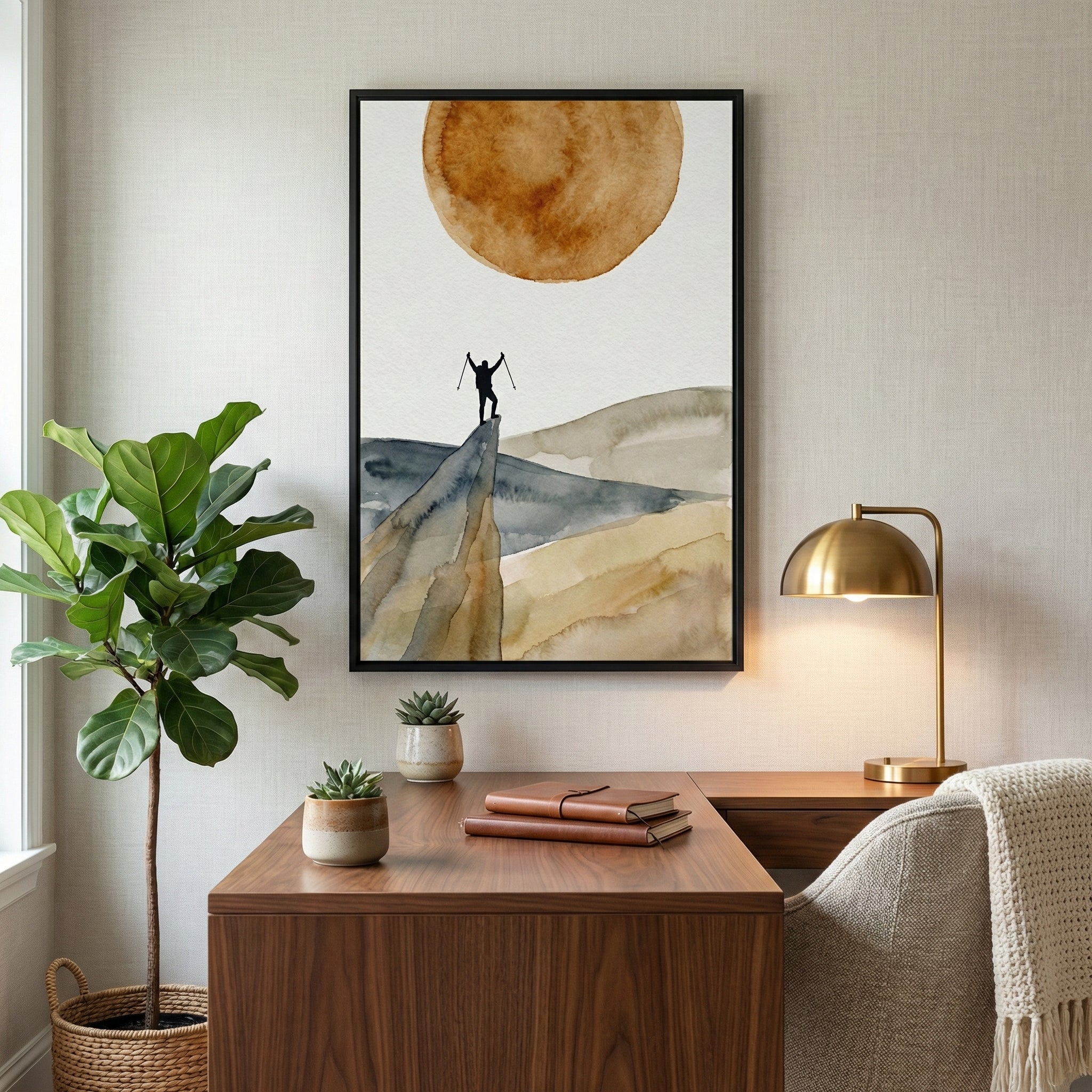 Framed artwork of a hiker standing victoriously on a mountaintop beneath a radiant sun, symbolizing adventure and perseverance, displayed in a cozy and motivational home office space.