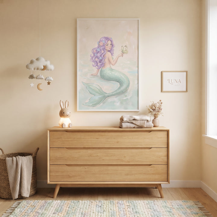 A wooden dresser sits below holding dainty butterfly mermaid wall art in a nursery with a hanging cloud mobile.