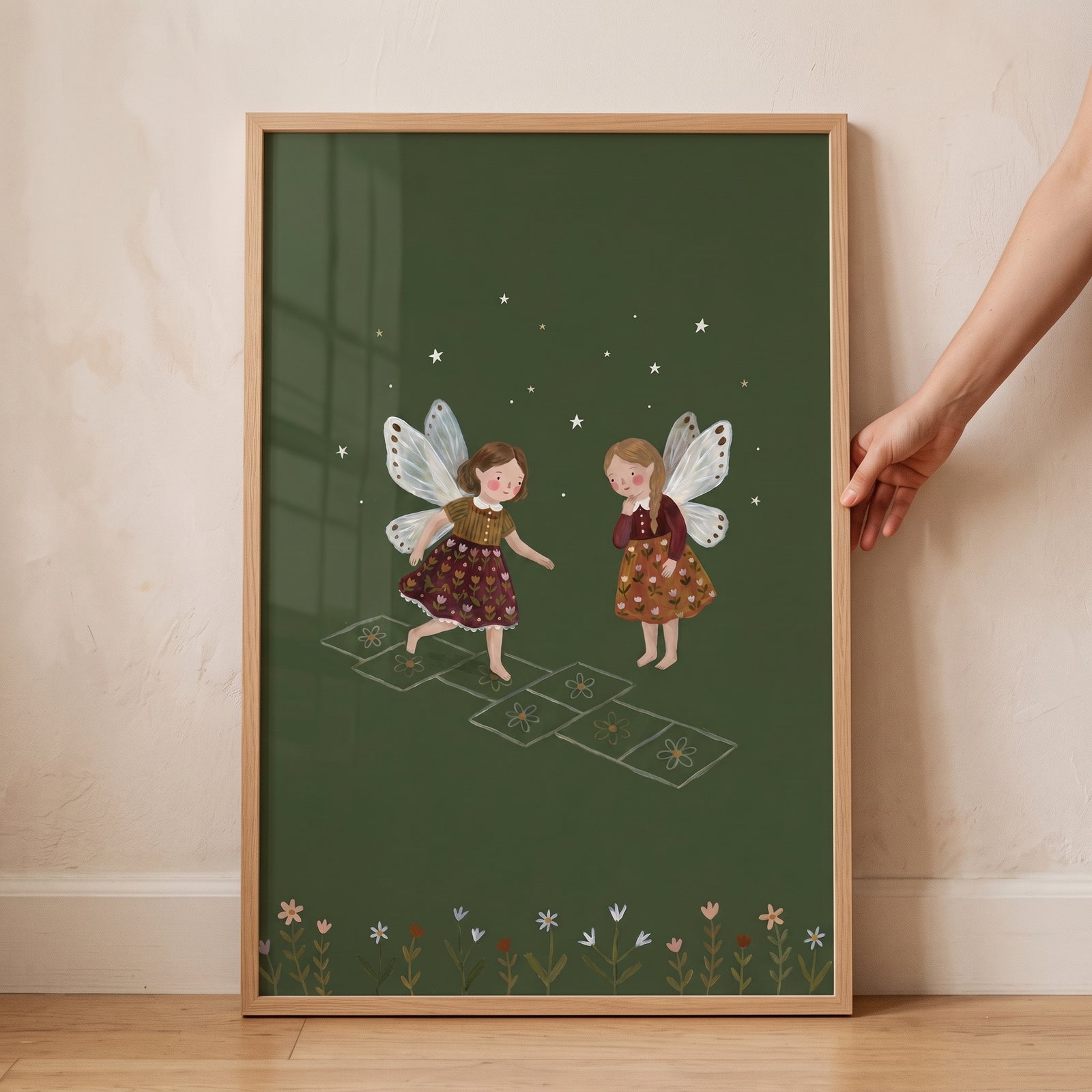 Two winged girls play on floral squares in this hopscotch playing garden fairies wall art with a green background.