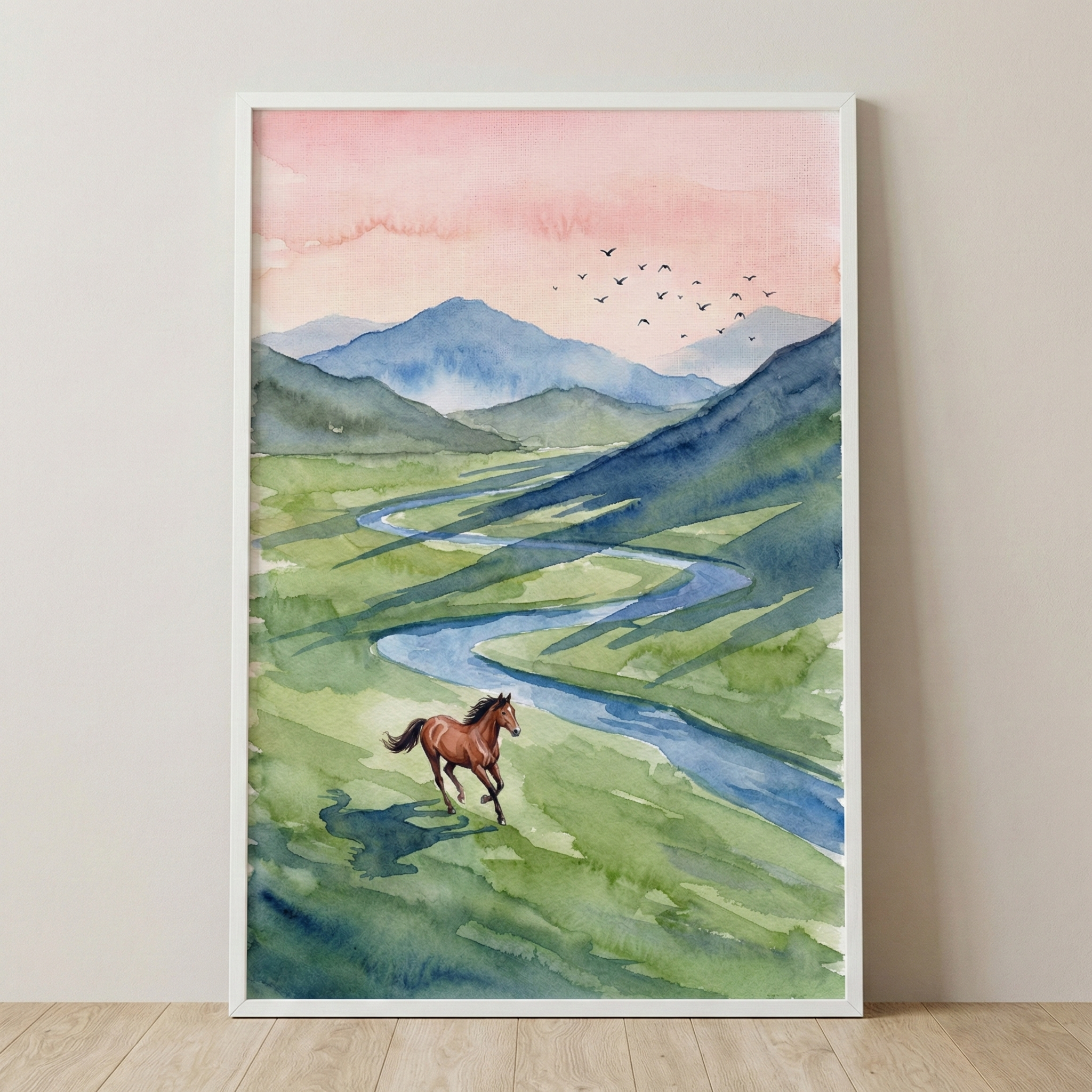 A vertical watercolor artwork captures a serene landscape with a brown horse galloping across a vibrant green valley. A winding blue river cuts through the grassy fields, and long, diagonal shadows suggest the low angle of a setting or rising sun. In the distance, layers of hazy blue mountains stand beneath a soft, peach-toned sky where a small flock of birds fly in formation. The composition is presented in a plain white frame, leaning against a neutral-toned wall on a light wood floor.